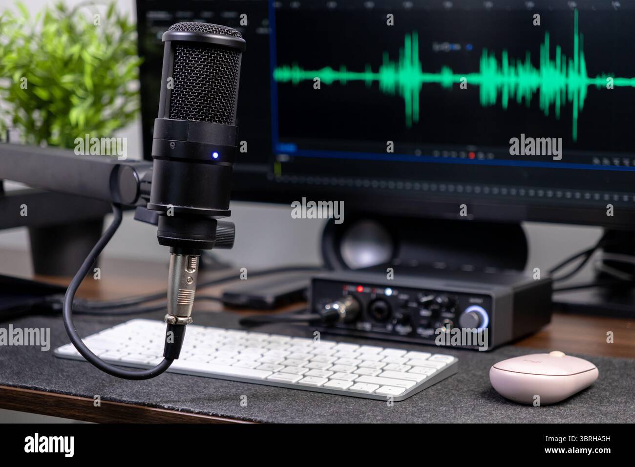 Configuration d'enregistrement audio moderne avec un microphone professionnel, une interface audio et un moniteur affichant les ondes sonores, parfait pour podcasting, streaming et Banque D'Images