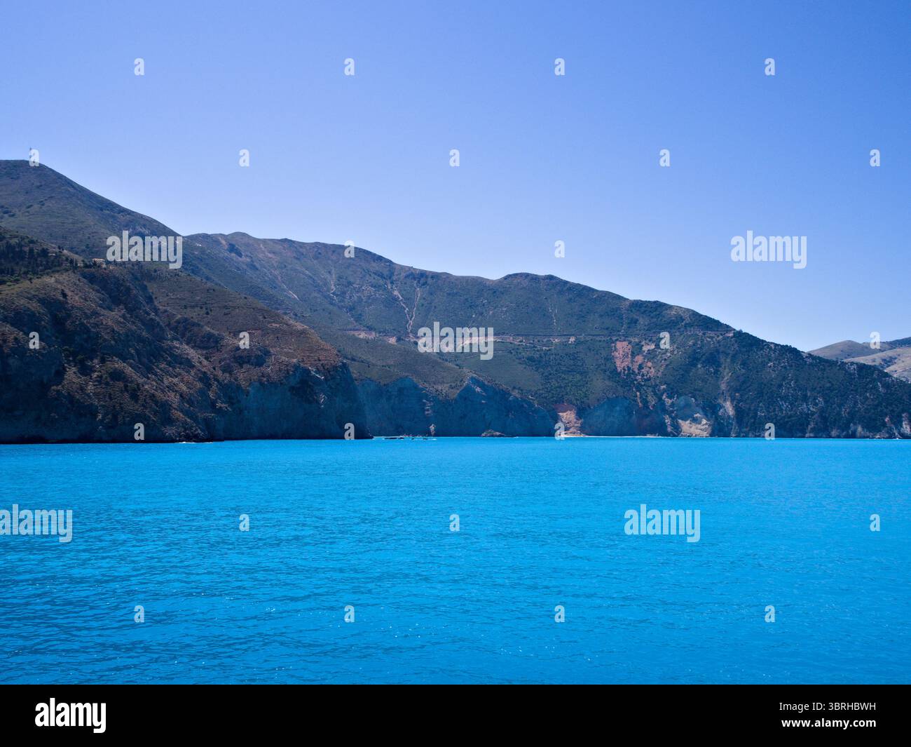 Vue panoramique sur la côte de l'île de Céphalonie avec des collines verdoyantes et des eaux turquoise vives sous un ciel méditerranéen clair. Banque D'Images