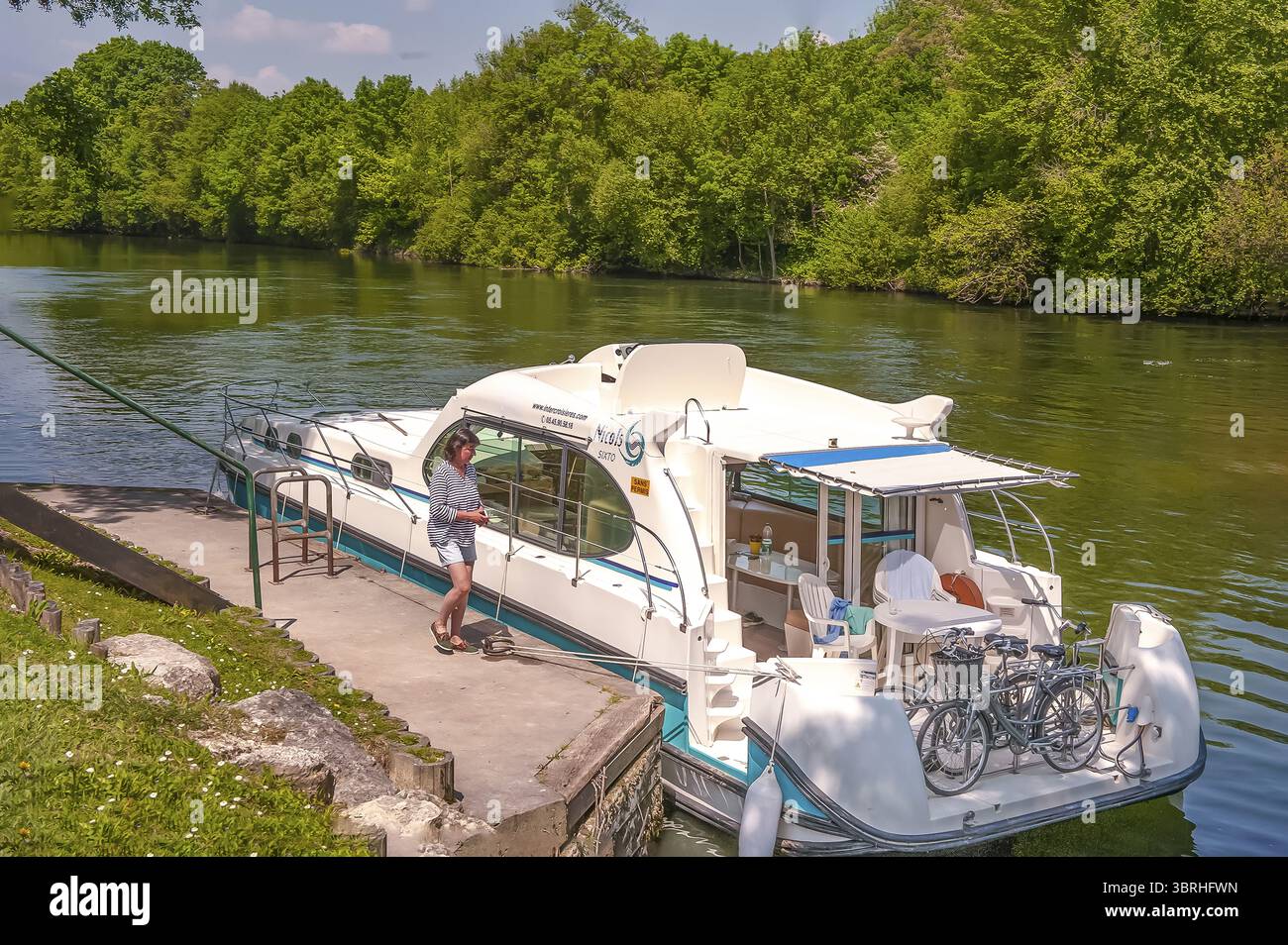 Femme marchant vers sa péniche transportant des vélos à la poupe à l'embarcadère de Gade-Moulin, rivière Charente, département de Charente, Nouvelle-Aquitaine, Fra Banque D'Images