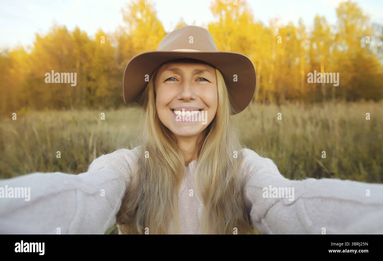 Gros plan portrait de femme mature souriante heureuse prenant selfie avec smartphone dans le parc d'automne, modèle féminin joyeux dans le chapeau à l'extérieur, saison d'automne Banque D'Images