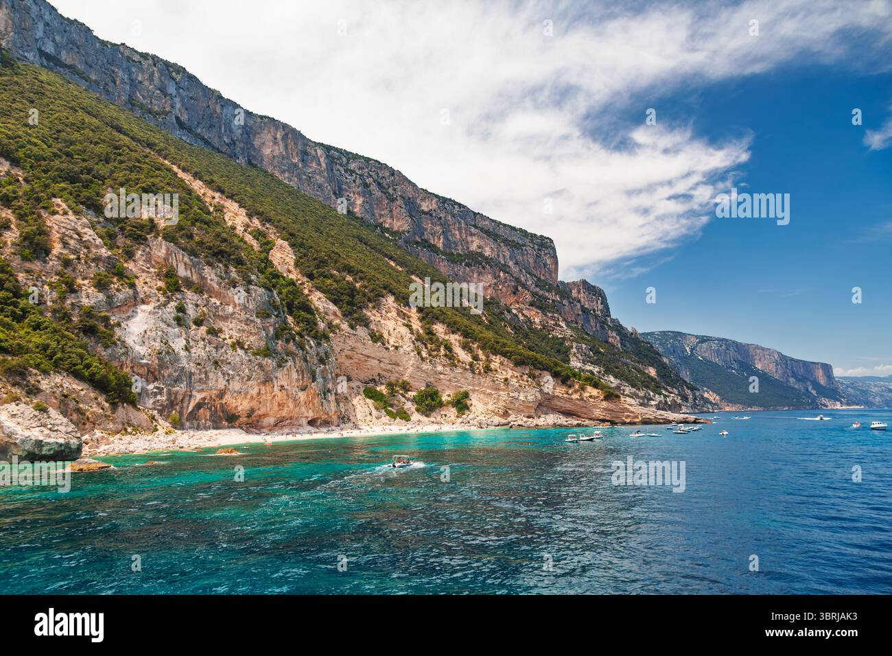Les bateaux flottent près de la côte turquoise sous les falaises abruptes et boisées le long du golfe d'Orosei sur la côte orientale de la Sardaigne en été Banque D'Images
