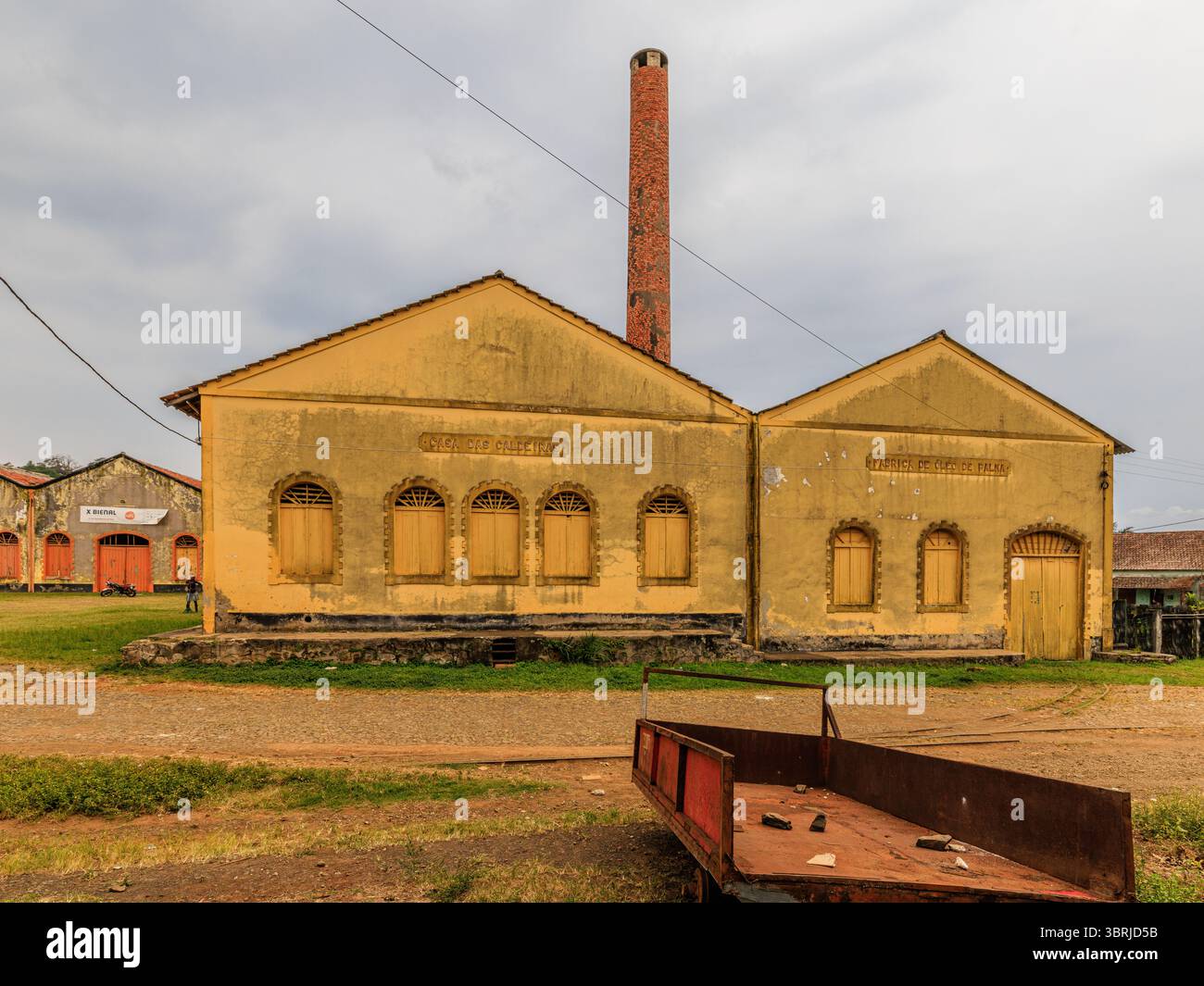 grande cheminée en brique au-dessus de deux grands bâtiments jaunes produisant de l'huile de palme et séchant des fèves de cacao à roca agua ize plantation coloniale sur sao tome Banque D'Images