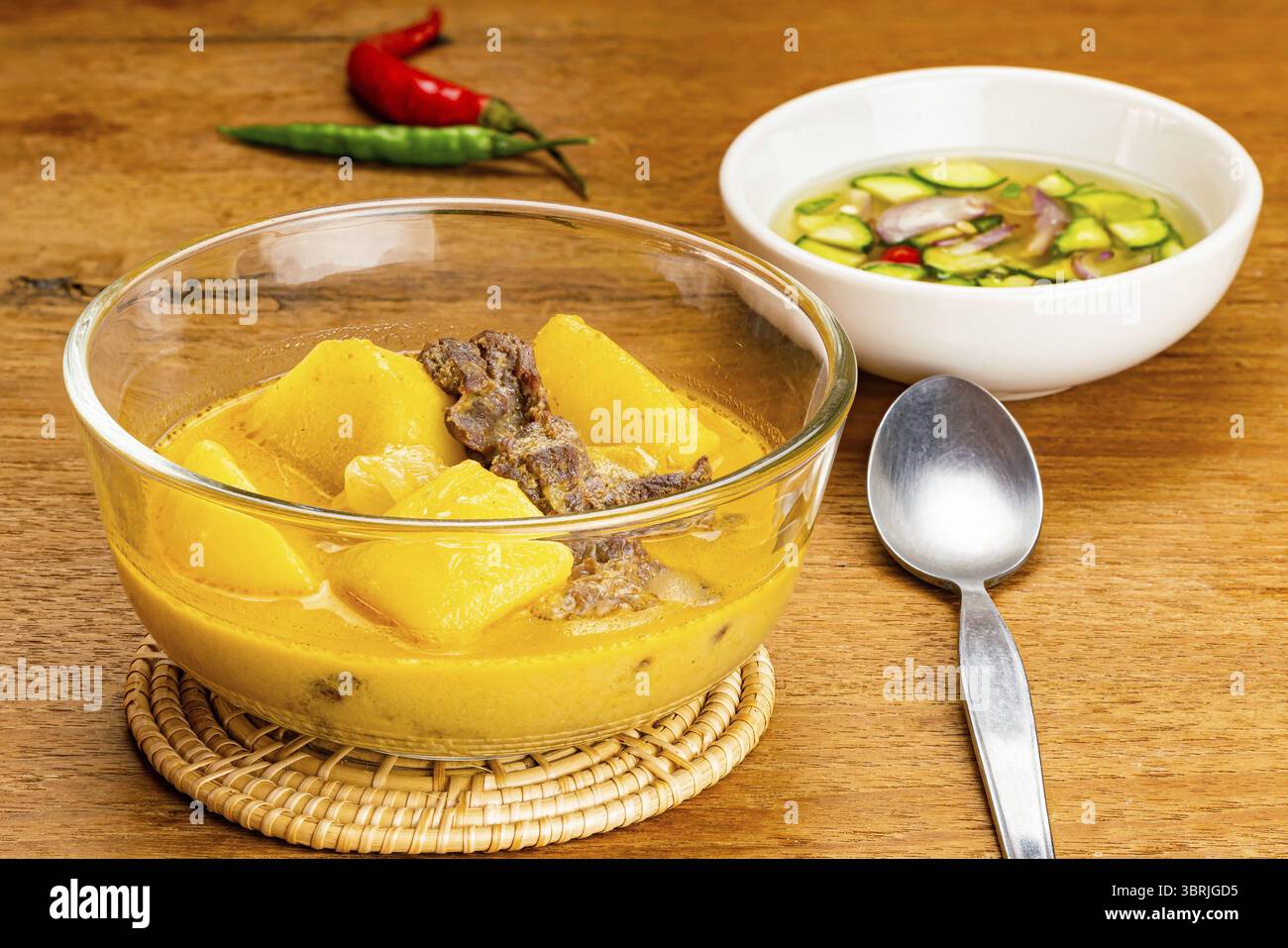 Délicieux curry traditionnel de pommes de terre, Chili, oignon de bœuf et lait de coco fait maison dans un bol en verre transparent sur un tapis de bambou avec une tranche de concombre, oignon, v Banque D'Images