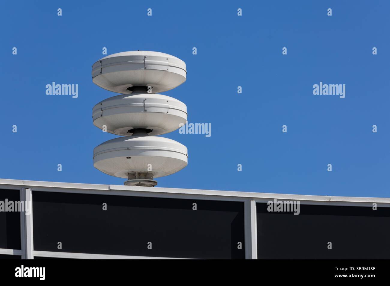 Un système de sirènes blanches empilées de la défense civile se trouve sur un bâtiment contre un ciel bleu clair, représentant la sécurité urbaine et les systèmes d'alerte. Banque D'Images