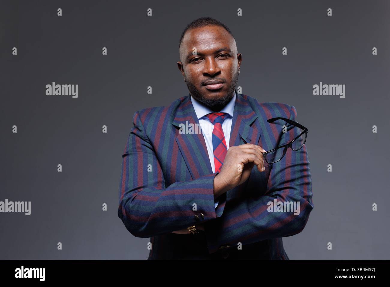 Portrait d'un homme d'affaires africain en costume élégant tenant des lunettes, montrant la confiance et le leadership dans les affaires Banque D'Images