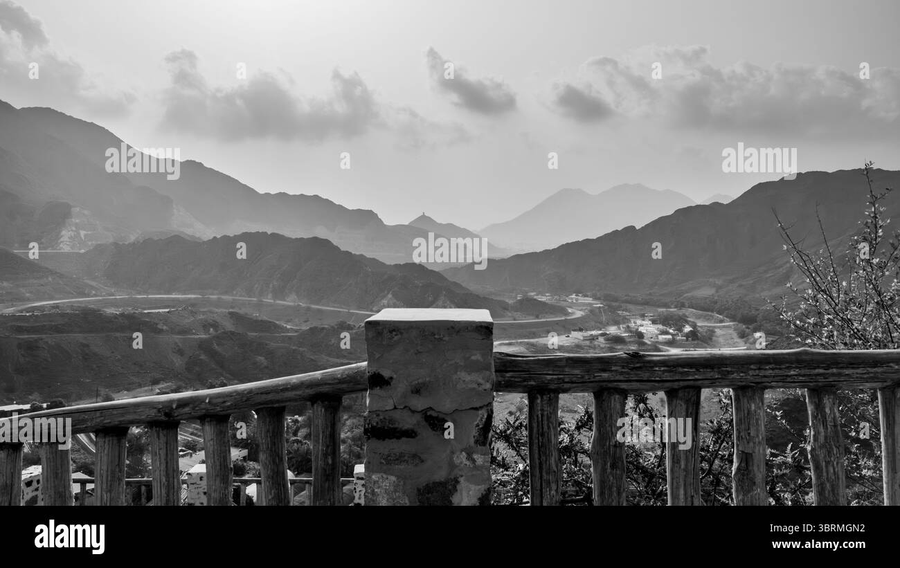 Un paysage de montagne pittoresque avec des sommets lointains sous un ciel nuageux, vu d'une clôture en bois Banque D'Images
