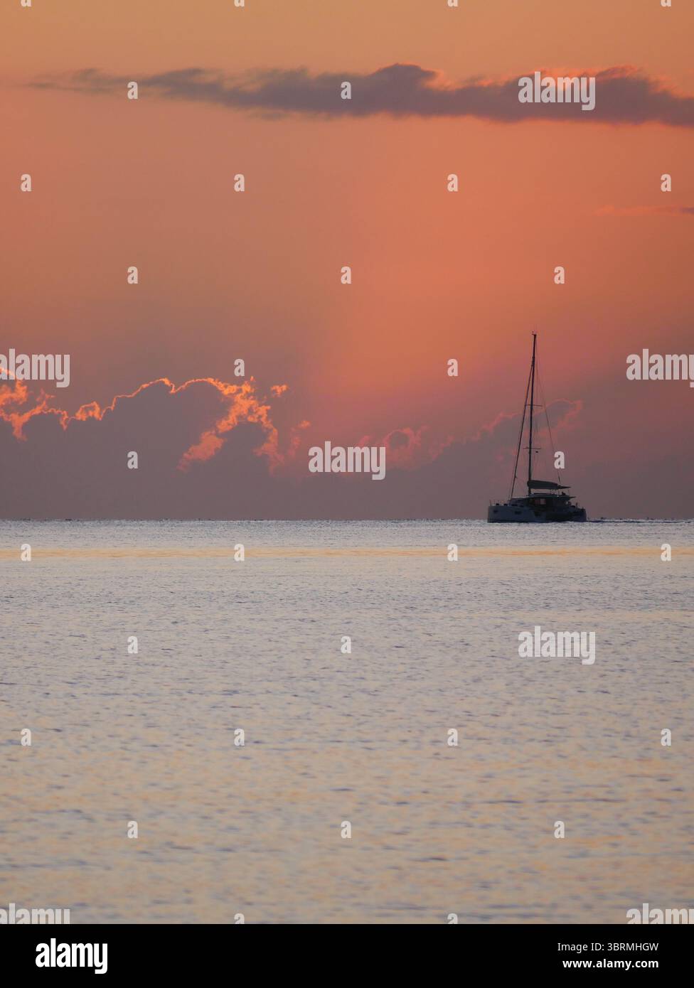 Un coucher de soleil à couper le souffle sur la mer calme avec un voilier à l'horizon. Des tons chauds orange et dorés remplissent le ciel et se reflètent sur l'eau. Voyage, na Banque D'Images