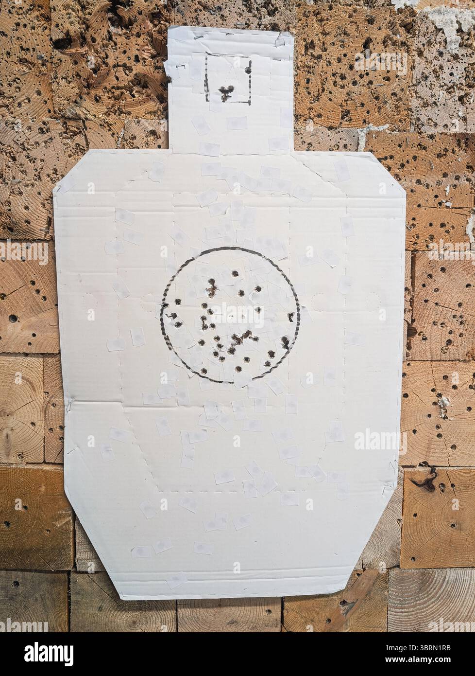 Cible en carton à silhouette humaine avec des trous de balle contre un piège à balles en bois sur un stand de tir. Banque D'Images