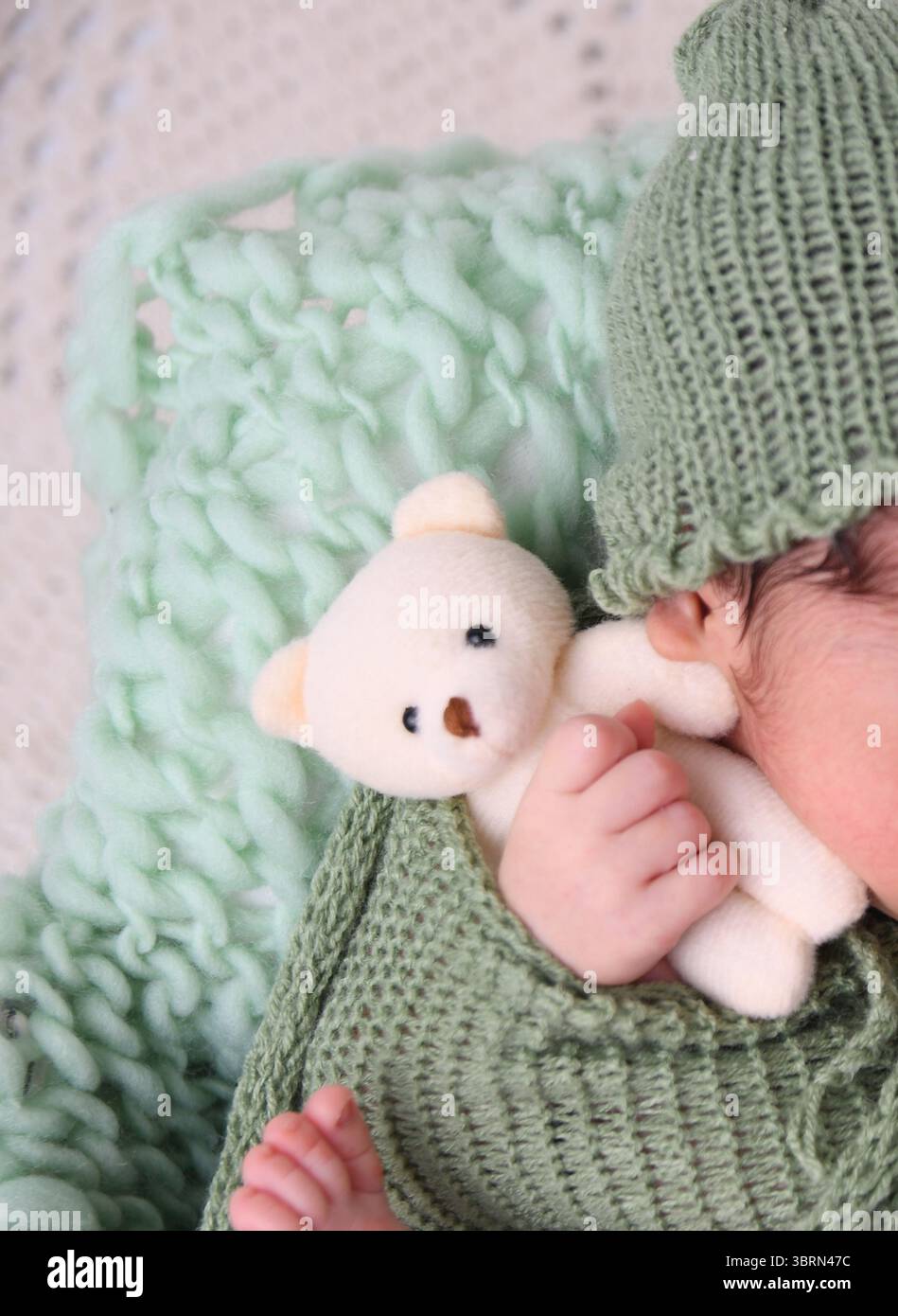 Gros plan de pieds de bébé enveloppés dans une couverture tricotée verte douce – concept nouveau-né Banque D'Images