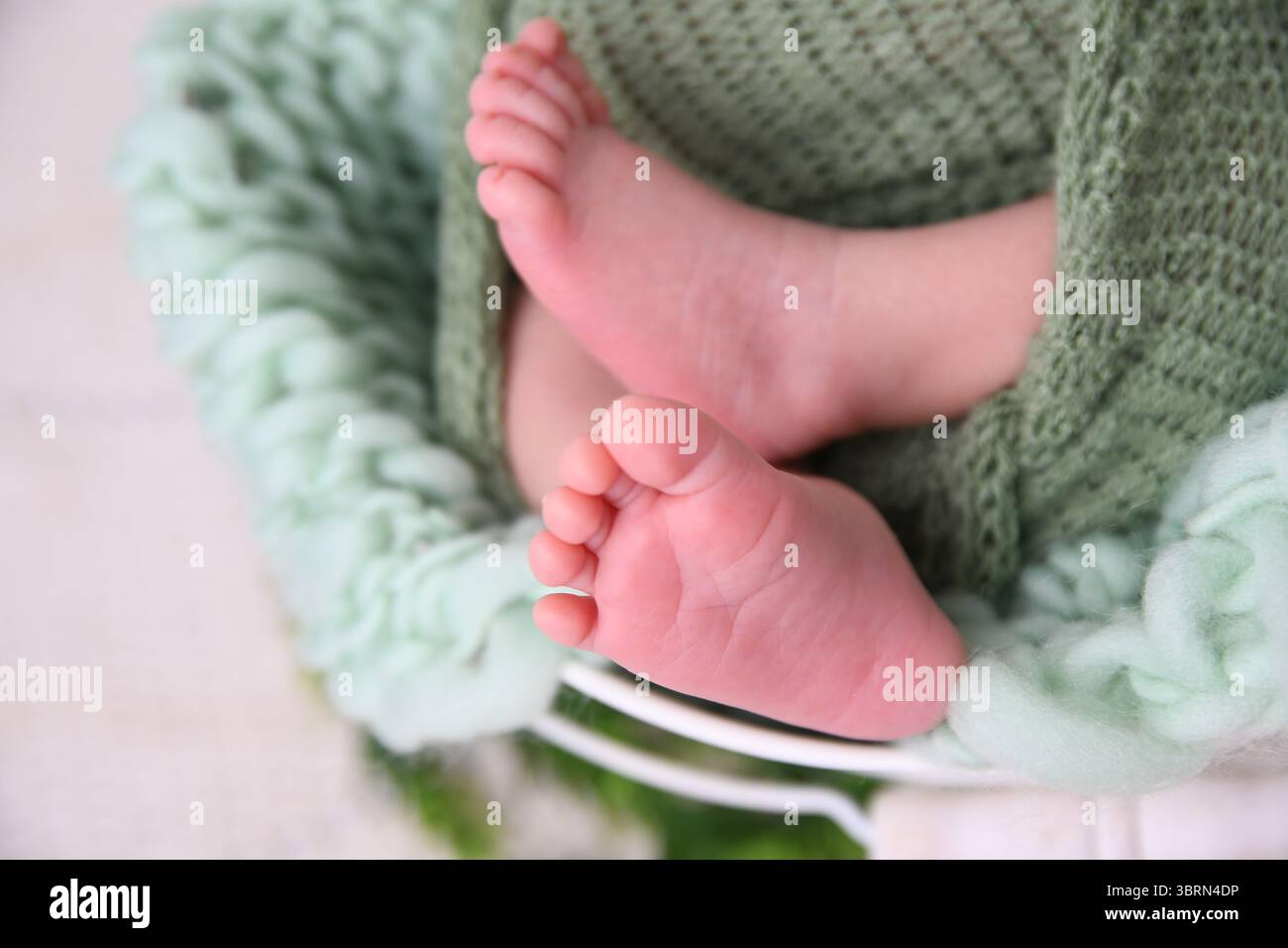 Gros plan de pieds de bébé enveloppés dans une couverture tricotée verte douce – concept nouveau-né Banque D'Images