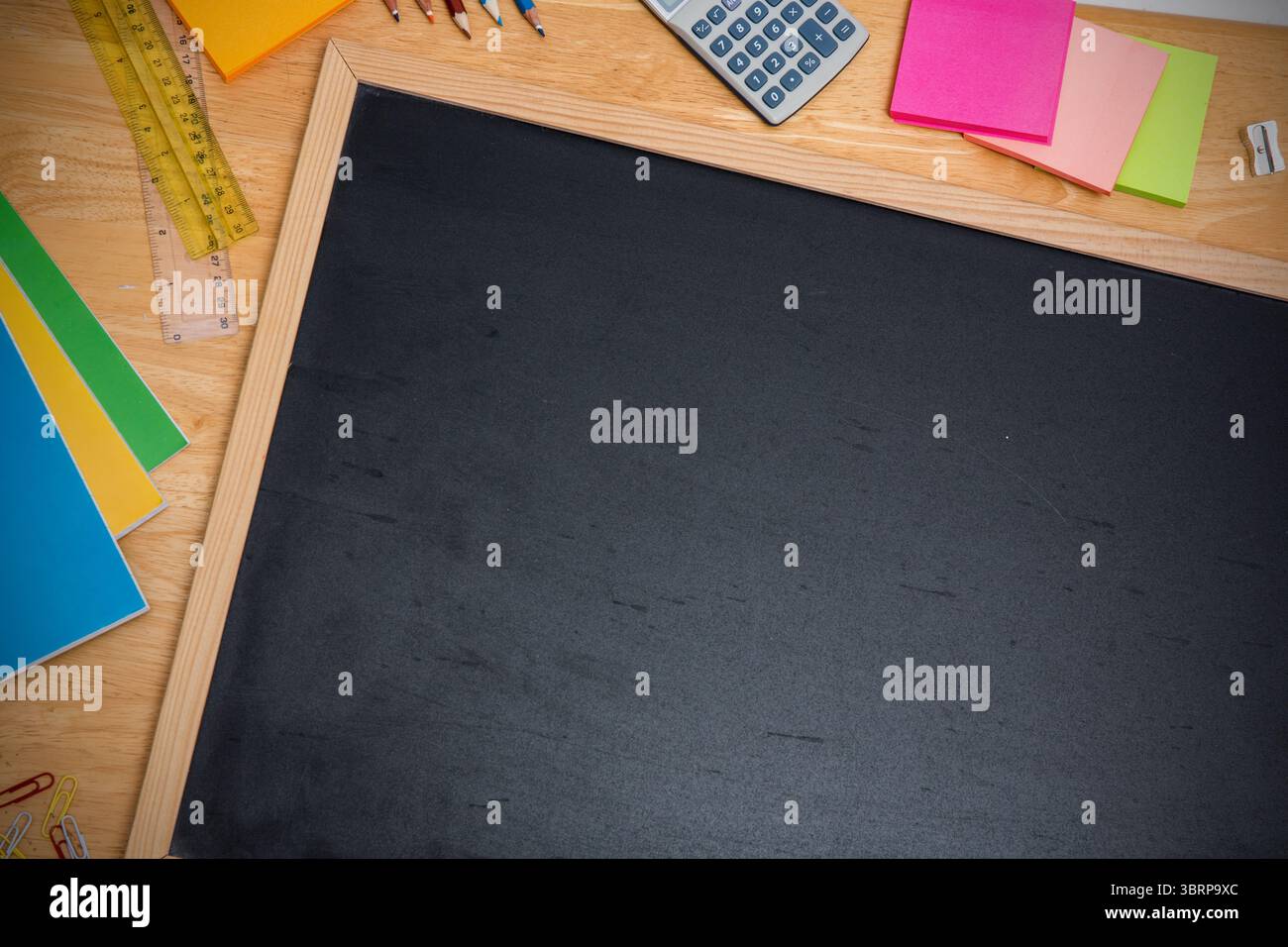 Tableau noir vierge est montré sur le bureau dans un design plat avec des crayons de couleur, des cahiers empilés, des règles Banque D'Images