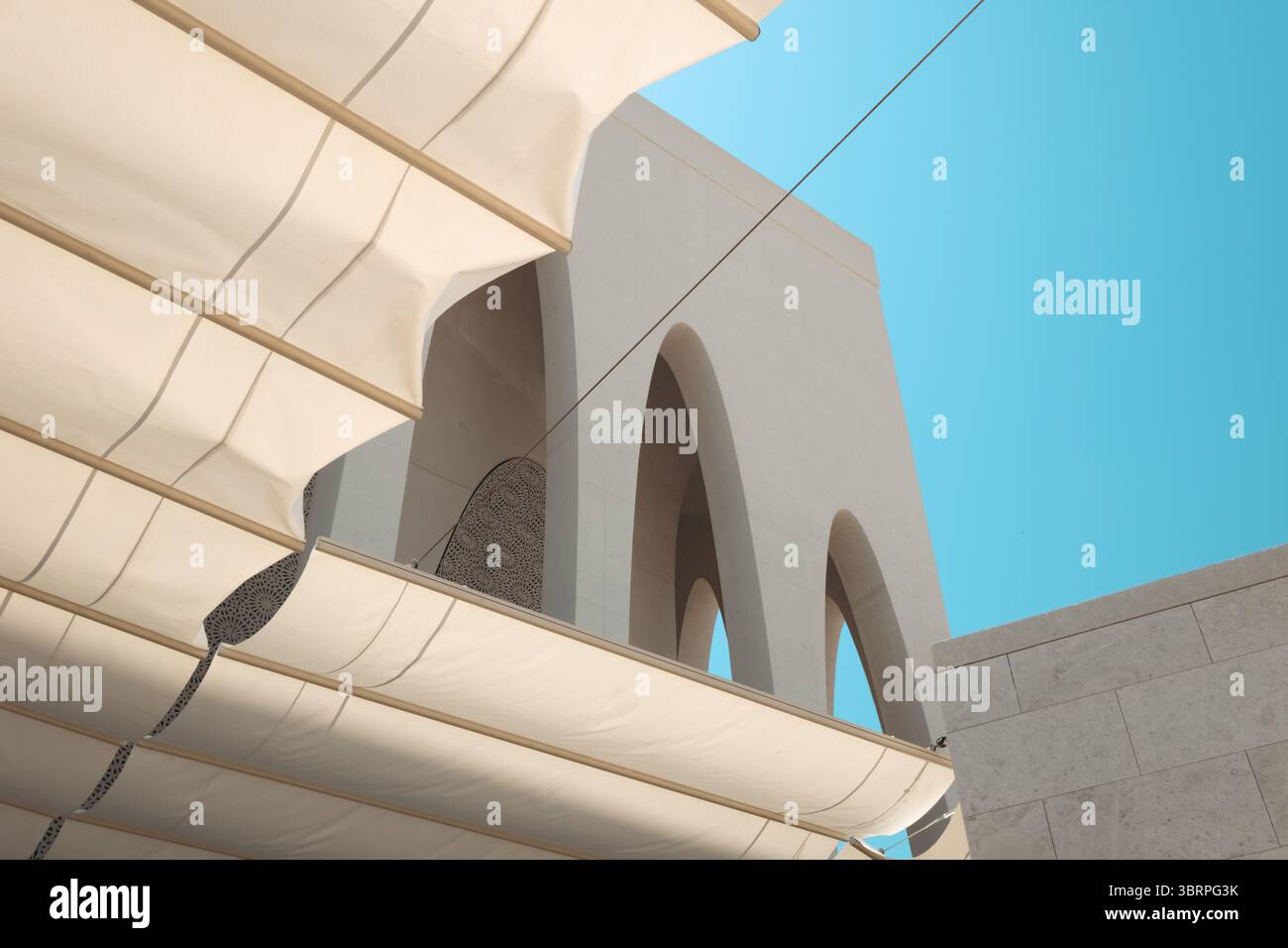 Une structure architecturale moderne avec de grandes arches, vue sous des auvents en tissu blanc contre un ciel bleu clair, fond d'architecture abstraite Banque D'Images
