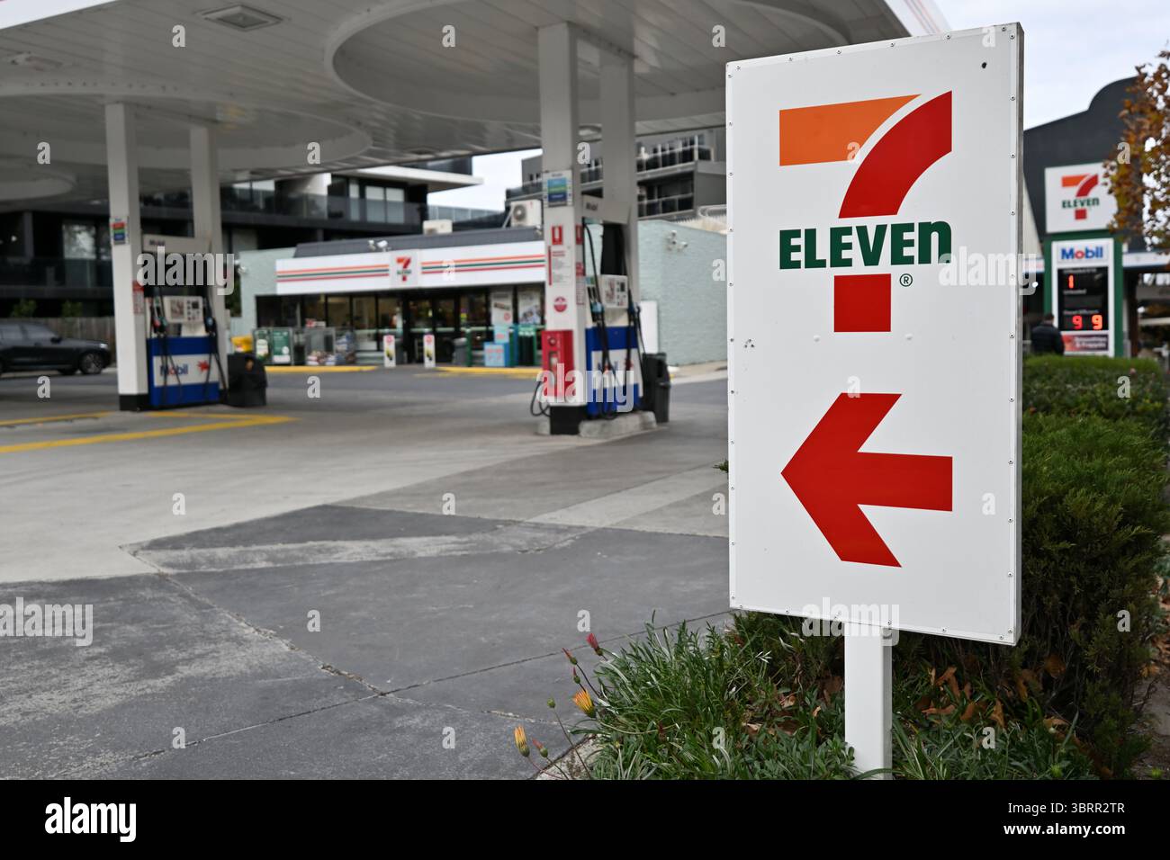 Panneau 7-Eleven, avec le logo de la société et une grande flèche rouge, à l'entrée du dépanneur et de la station-service Mobil attenante Banque D'Images