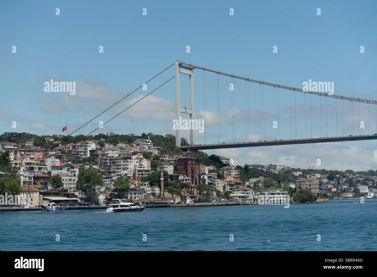 Une perspective pittoresque d'un pont traversant le Bosphore, mettant en valeur les maisons colorées du front de mer d'Istanbul et un ciel bleu vif. Banque D'Images