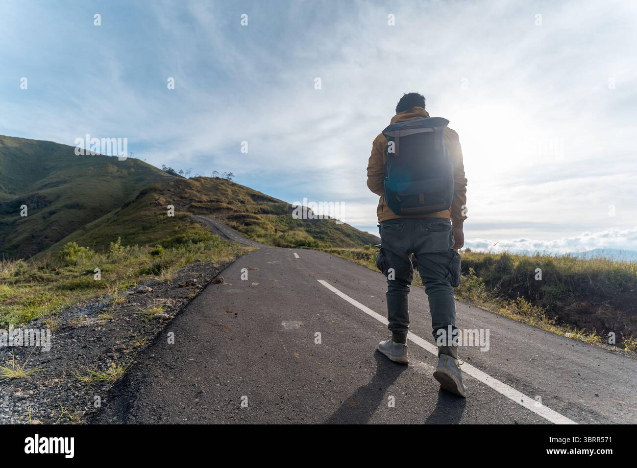 Randonneur avec sac à dos grimpant la route de montagne raide sous le soleil du matin. Banque D'Images