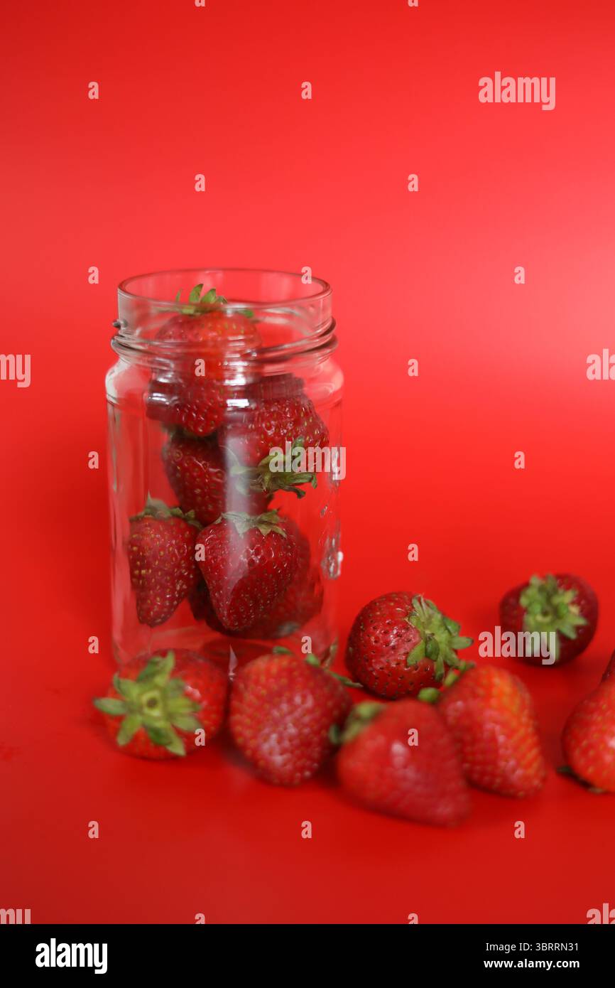 Pot en verre transparent de fraises biologiques saines sur Rouge Banque D'Images
