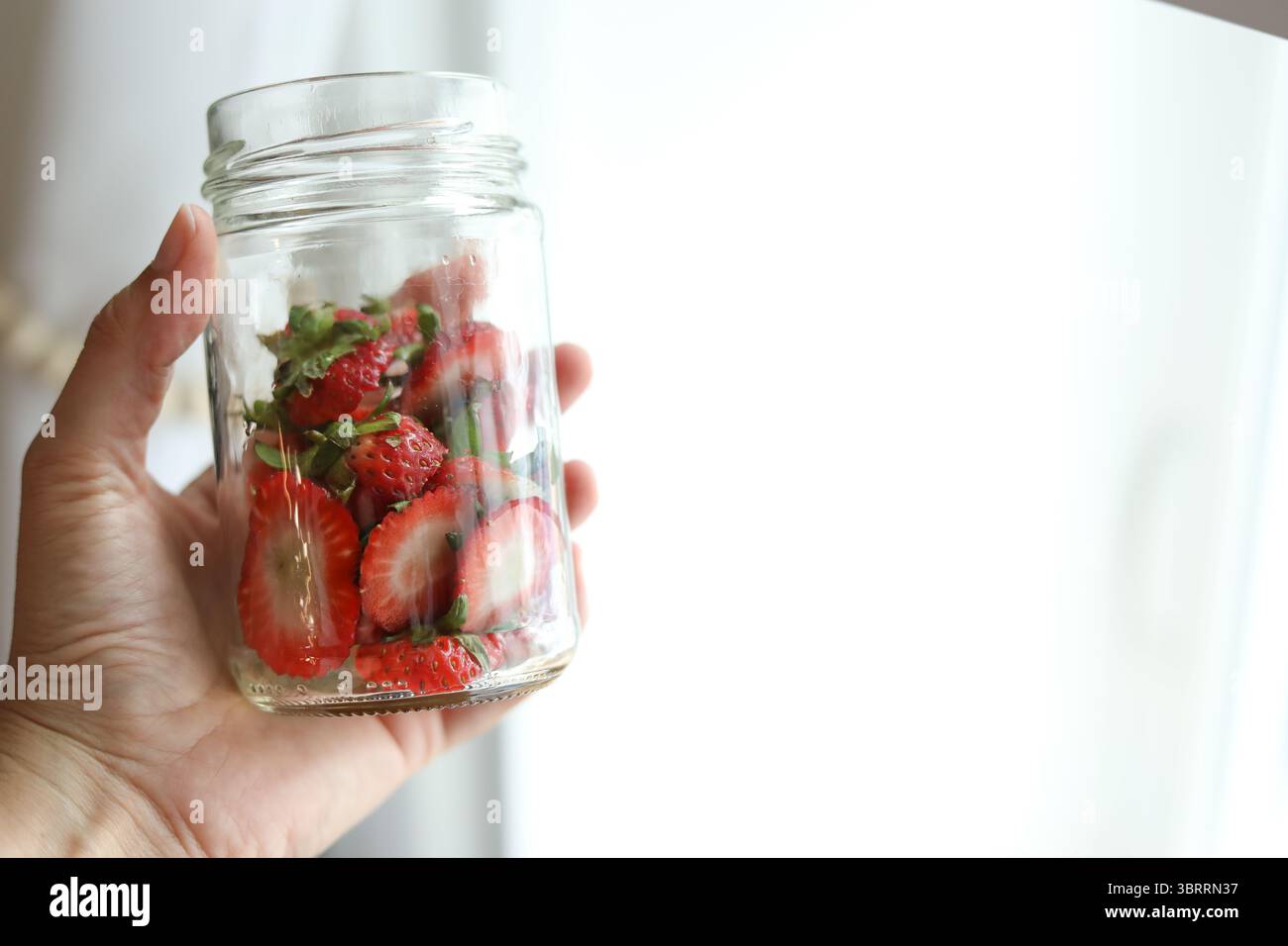 Main tenant un pot en verre transparent de dessus de fraises Banque D'Images