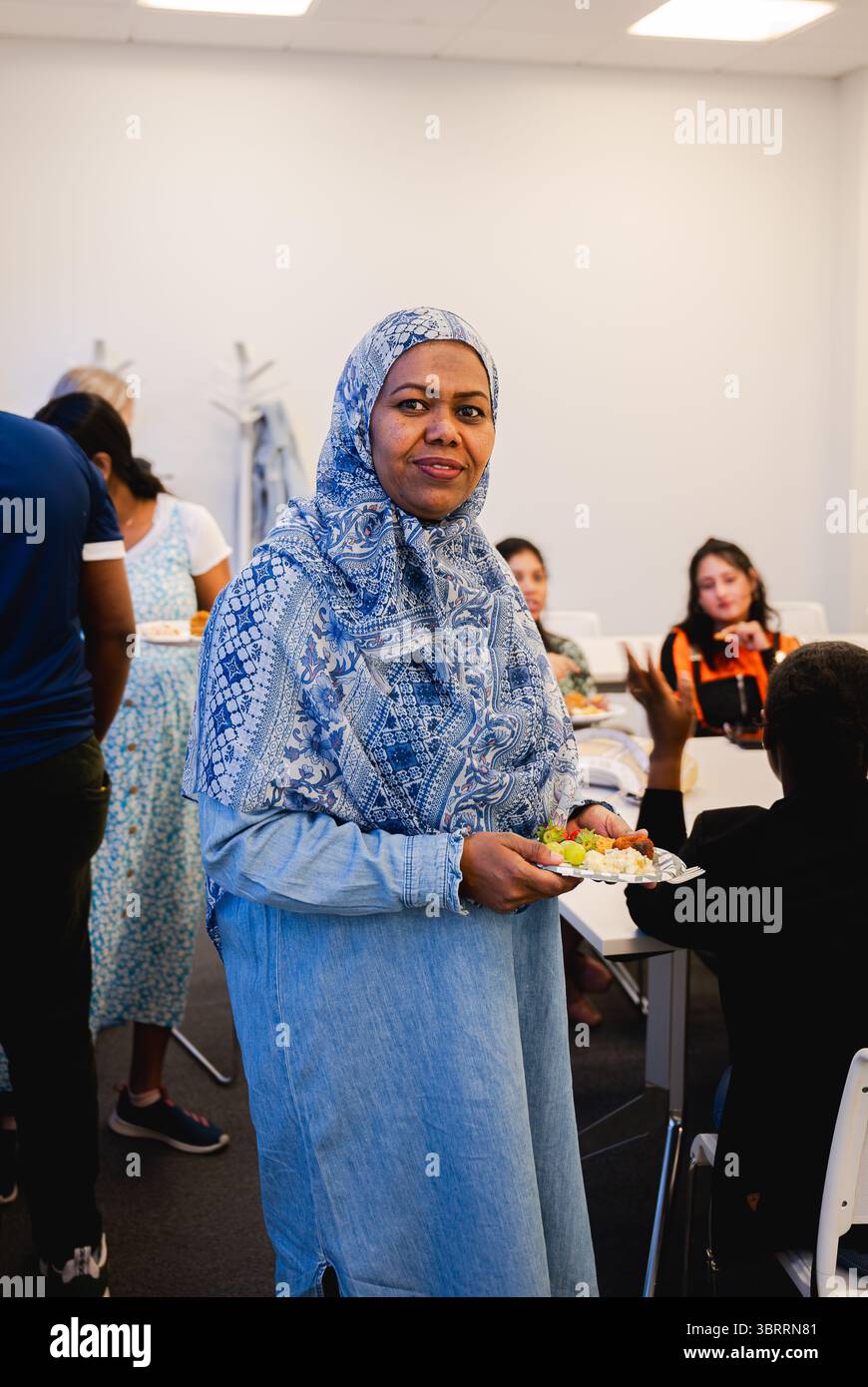 Femme musulmane en hijab tenant une assiette de nourriture pendant le déjeuner de bureau Banque D'Images