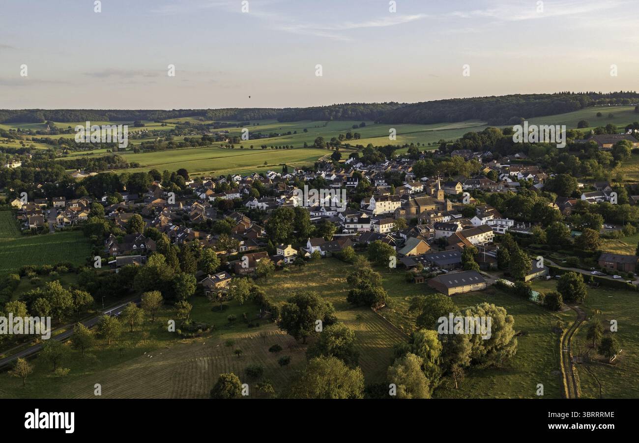 Vue aérienne d'un village pittoresque niché parmi les collines verdoyantes, où les toits jettent un œil à travers des arbres luxuriants sous un ciel doux et vaste., Epen, Limbourg, pays-Bas. Banque D'Images