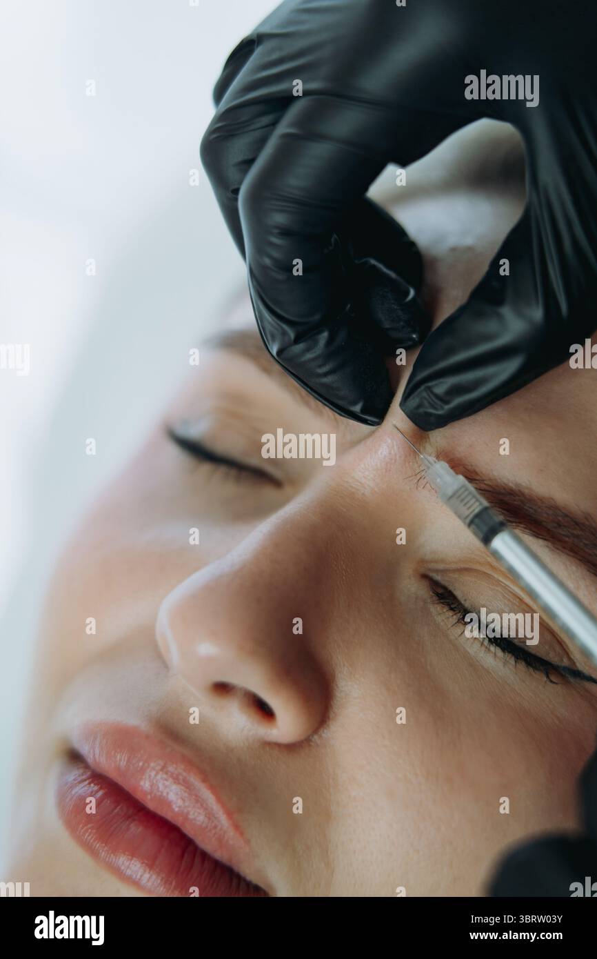 Gros plan de mains professionnelles faisant ingection de Botox dans la ligne de sourcils de femme Banque D'Images