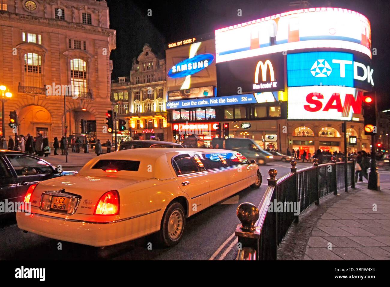 Limousine de luxe extensible dans le West End de Londres transportant des passagers en visite dans la circulation nocturne hivernale très fréquentée en circulant autour du célèbre carrefour routier Piccadilly Circus et du lieu de rassemblement populaire dominé par des panneaux publicitaires lumineux éclectiques en couleur dans la ville de Westminster Londres Angleterre Royaume-Uni image nocturne de l'année 2000. Banque D'Images