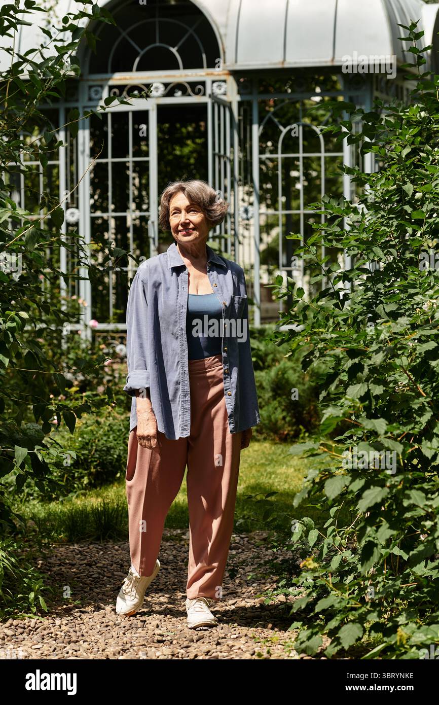 Une femme âgée avec grâce marche le long d'un chemin tranquille dans un jardin florissant, profitant de la nature. Banque D'Images