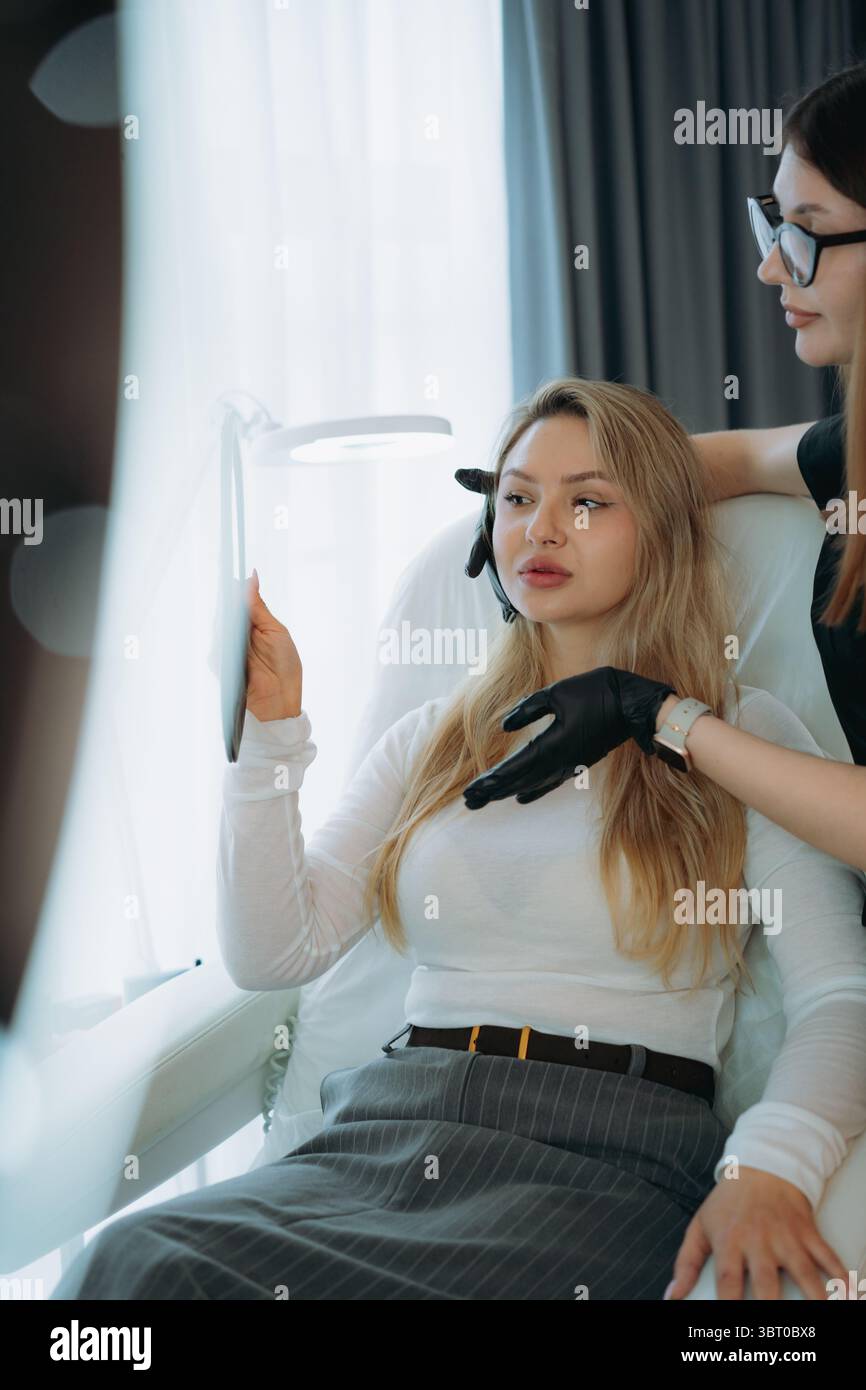 femme médecin esthétique à la consultation personnalisée anti-âge avec une jeune cliente tenant un miroir Banque D'Images