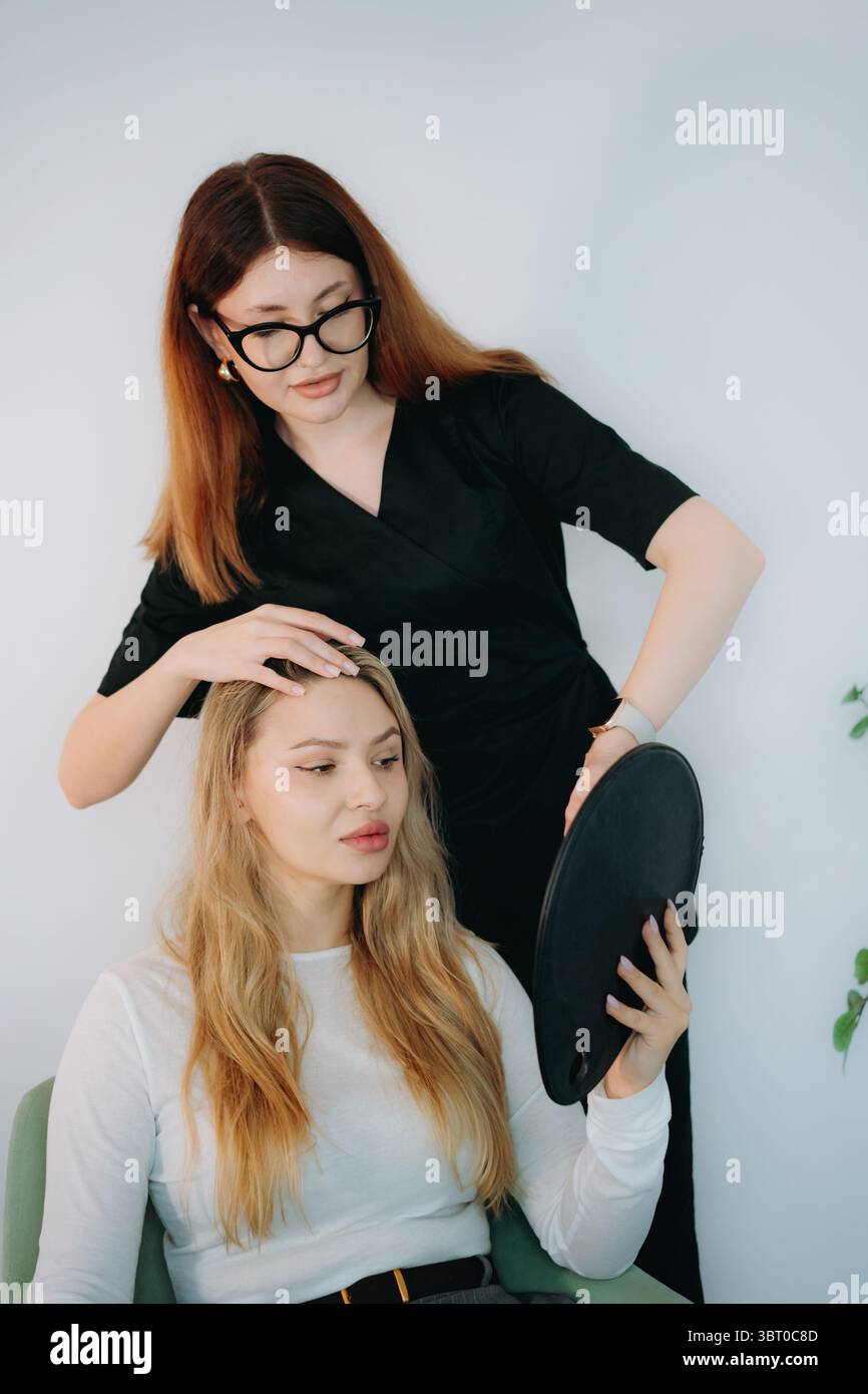femme médecin esthétique à la consultation personnalisée anti-âge avec une jeune cliente tenant un miroir Banque D'Images