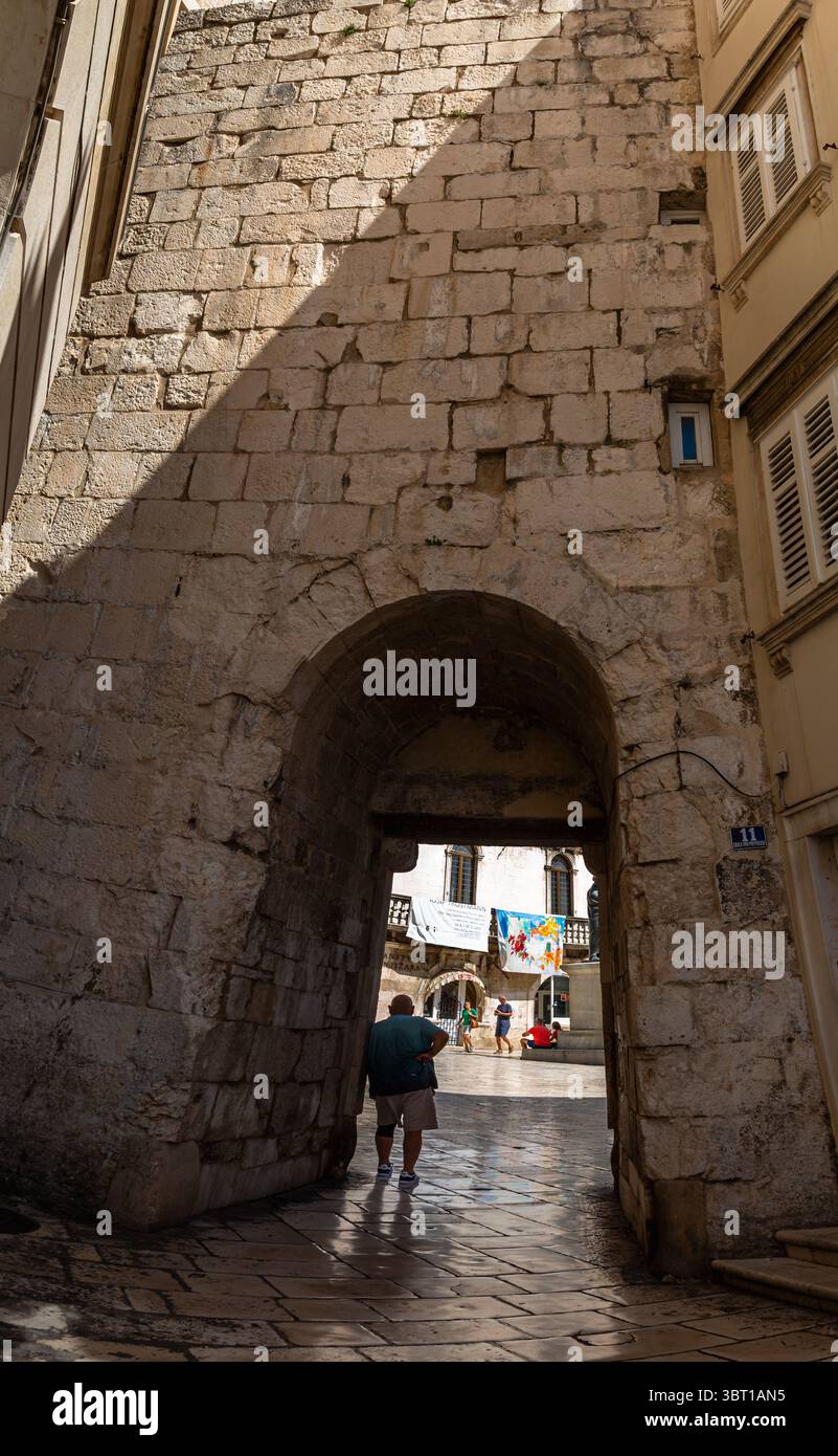 Split, Croatie - 8 septembre 2023 : un homme traverse une arche pour entrer dans une place. Les gens sont rassemblés sur la place. Banque D'Images
