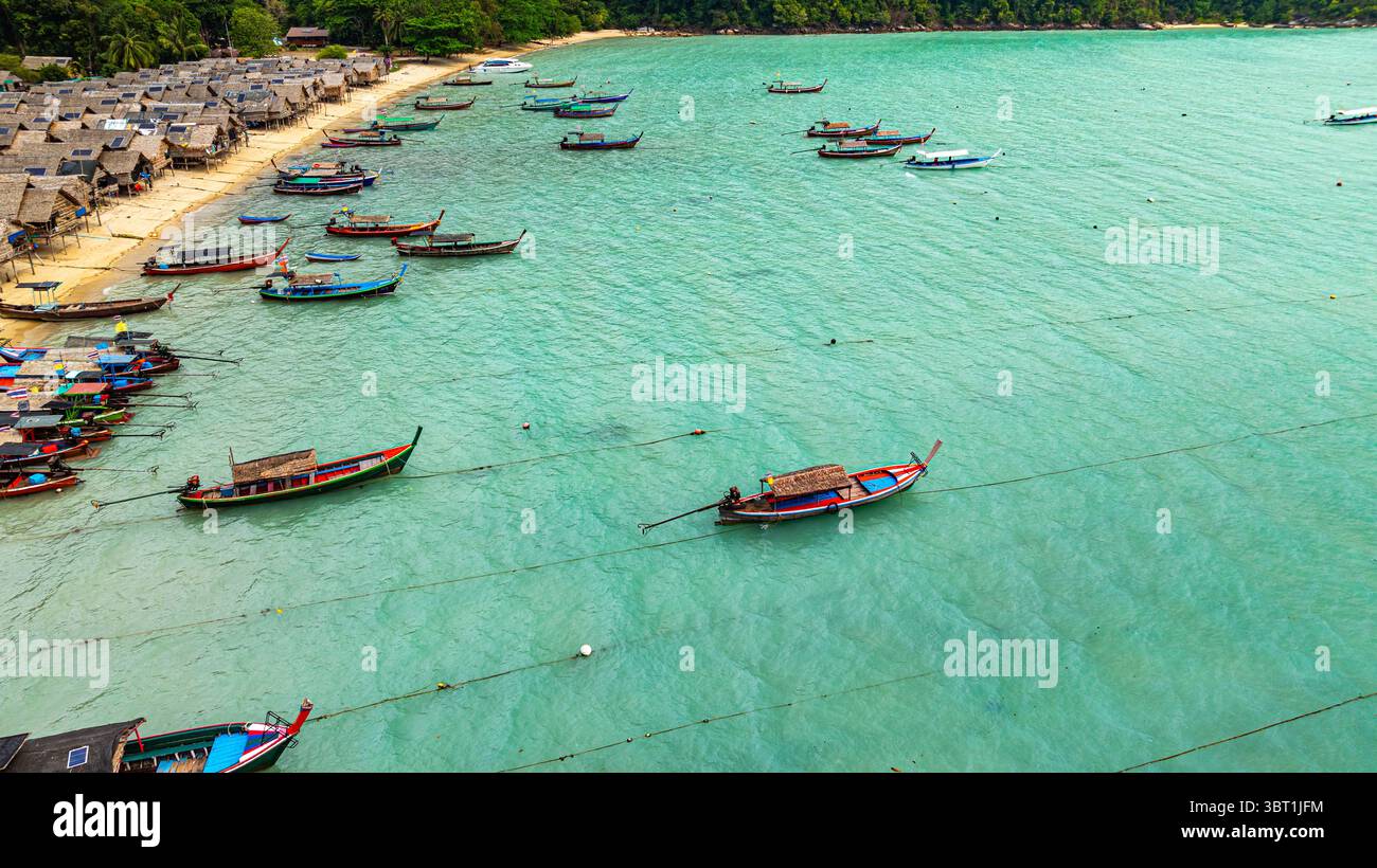 Une vue aérienne imprenable sur un village balnéaire tropical avec des rangées de petites cabanes le long du littoral, les bateaux de pêche traditionnels sont ancrés dans le turquois Banque D'Images