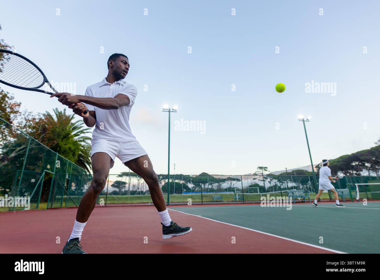 Adversaires masculins afro-américains et asiatiques frappant le revers sur le filet sur le court de tennis, espace de copie Banque D'Images