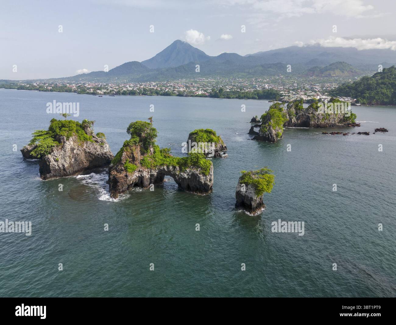 Vue aérienne des falaises escarpées de l'île de Bota et de la verdure vibrante rencontre l'océan, avec la ville et le Mont Cameroun au loin, Limbe, Sud-Ouest, Cameroun. Banque D'Images
