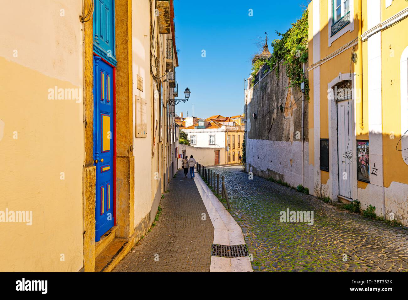 Rues pavées étroites devant des portes colorées et des bâtiments dans le quartier médiéval Alfama à flanc de colline de Lisbonne, Portugal. Banque D'Images