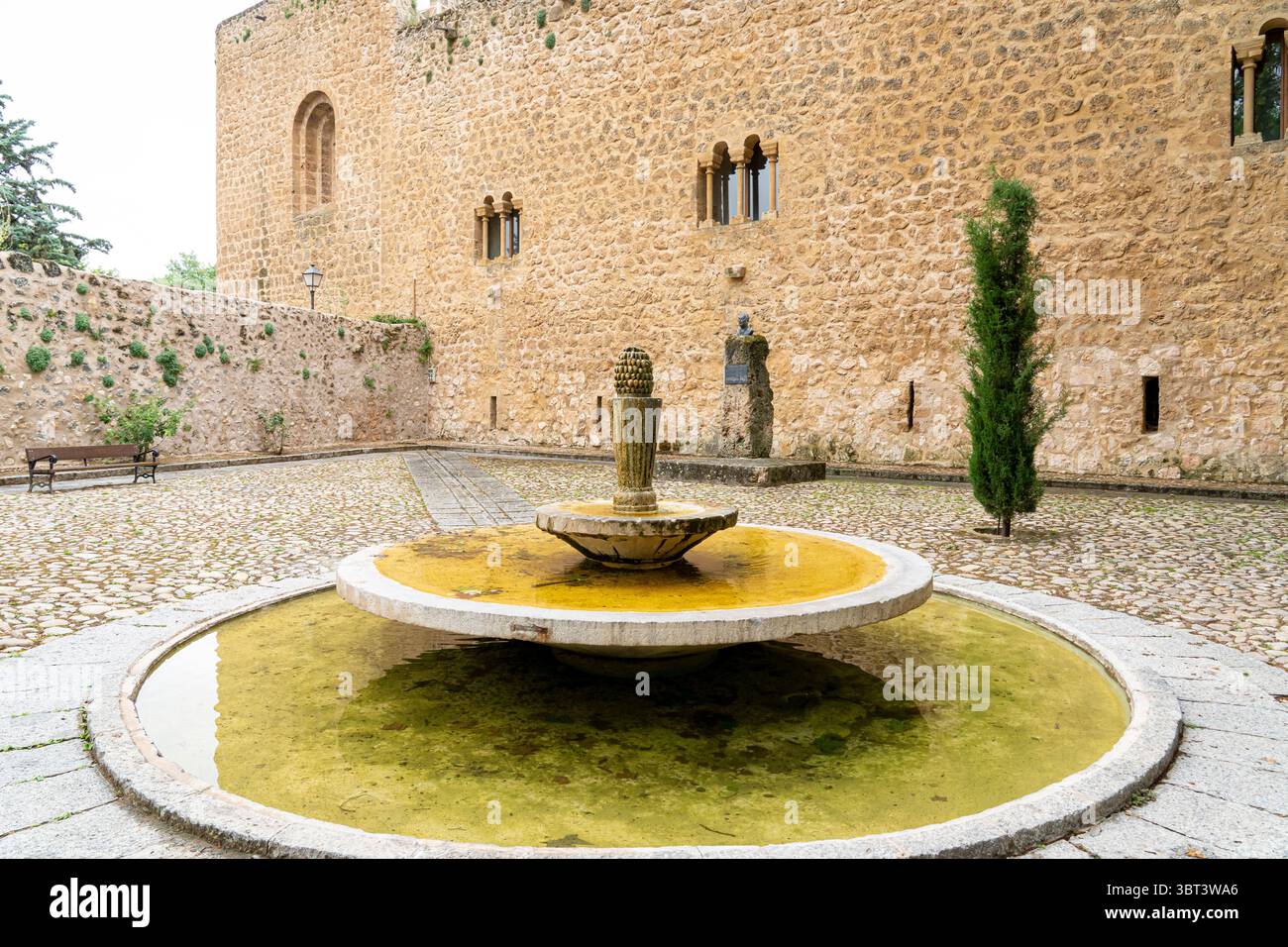 Une cour tranquille avec une fontaine circulaire entourée de murs de pierre historiques à Brihuega, mettant en valeur la riche architecture et atmosphère sereine Banque D'Images