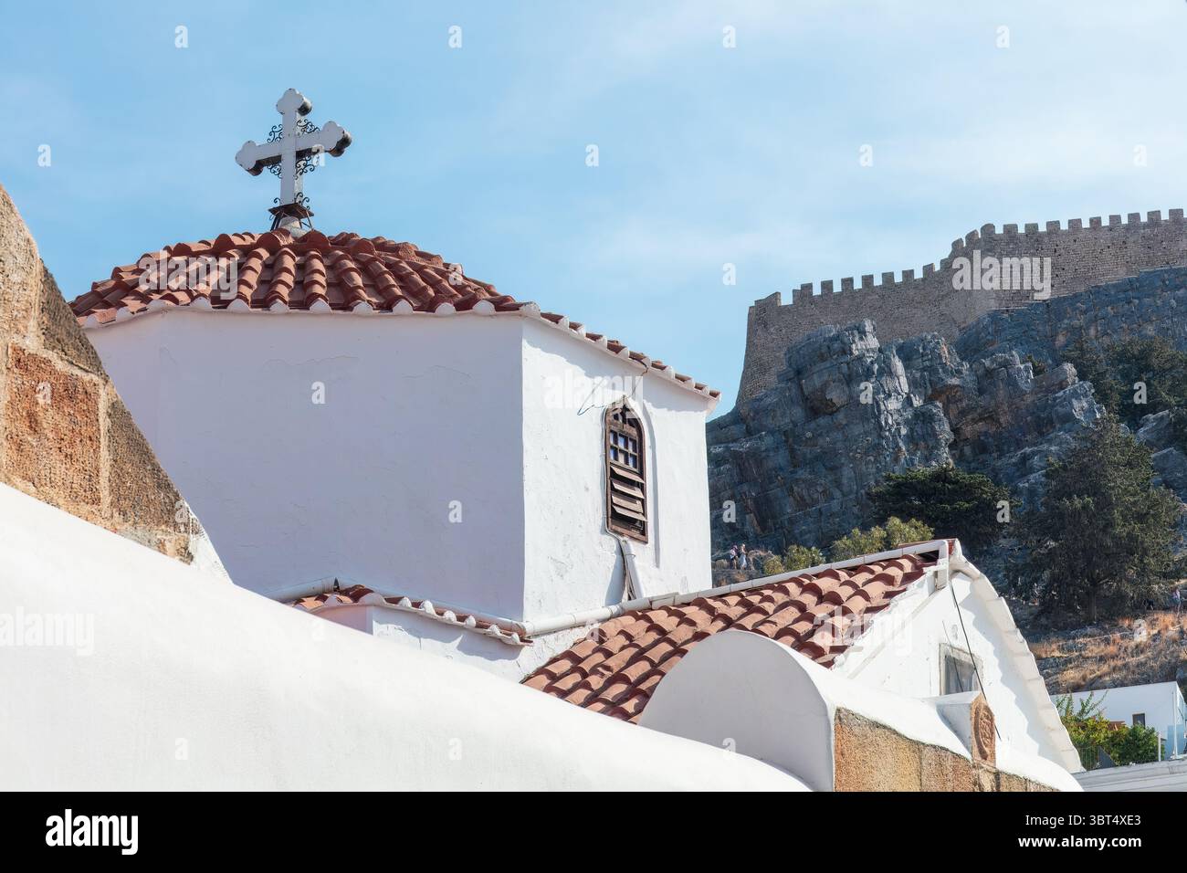 Rhodes, Grèce - 15 octobre 2024 : église blanchie à la chaux avec toit en tuiles rouges et croix, face à l'Acropole de Lindos à Rhodes, Grèce. Méditerranée Banque D'Images