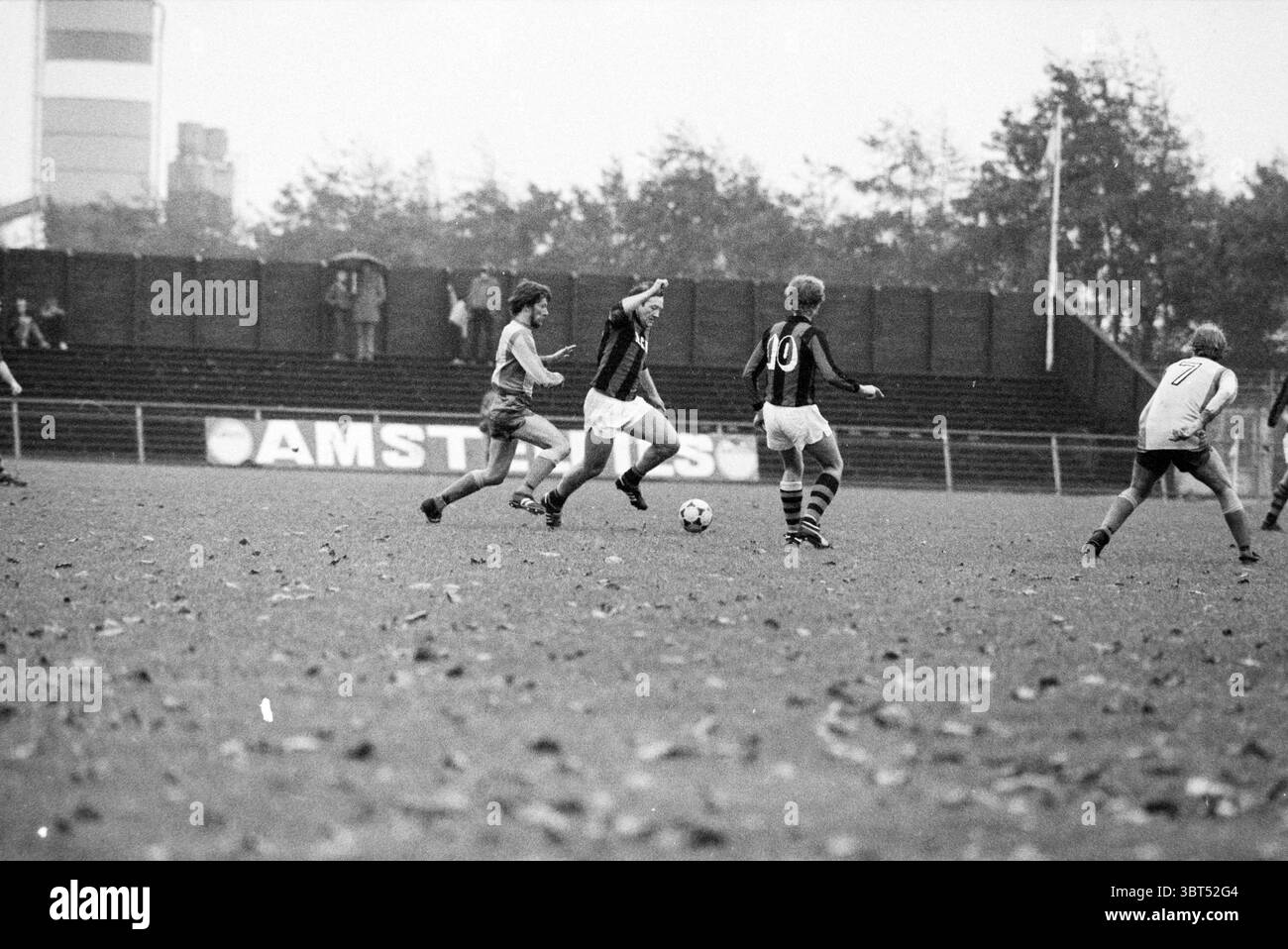 RCH - AFC 34 Football R.C.H., Whizgle News, Dutch Desk, pays-Bas, 1950 - 2000 on 26-10-1980. Voici les rubriques de l'image. La scène se déroule sur un terrain de football dynamique, où l'herbe est d'un vert profond, tachetée de feuilles tombées qui ont pris des nuances de jaune et de brun, suggérant le début de l'automne. L'atmosphère est un peu nuageuse, avec un ciel gris qui fait allusion à la pluie récente, créant une ambiance un peu silencieuse. Au premier plan, deux équipes sont engagées dans un jeu dynamique. D'un côté, un joueur portant un maillot sombre et à motifs avec des rayures audacieuses vient de recevoir le ballon, présentant un f Banque D'Images RCH - AFC 34 Football R.C.H., Whizgle News, Dutch Desk, pays-Bas, 1950 - 2000 on 26-10-1980. Voici les rubriques de l'image. La scène se déroule sur un terrain de football dynamique, où l'herbe est d'un vert profond, tachetée de feuilles tombées qui ont pris des nuances de jaune et de brun, suggérant le début de l'automne. L'atmosphère est un peu nuageuse, avec un ciel gris qui fait allusion à la pluie récente, créant une ambiance un peu silencieuse. Au premier plan, deux équipes sont engagées dans un jeu dynamique. D'un côté, un joueur portant un maillot sombre et à motifs avec des rayures audacieuses vient de recevoir le ballon, présentant un f Banque D'Images