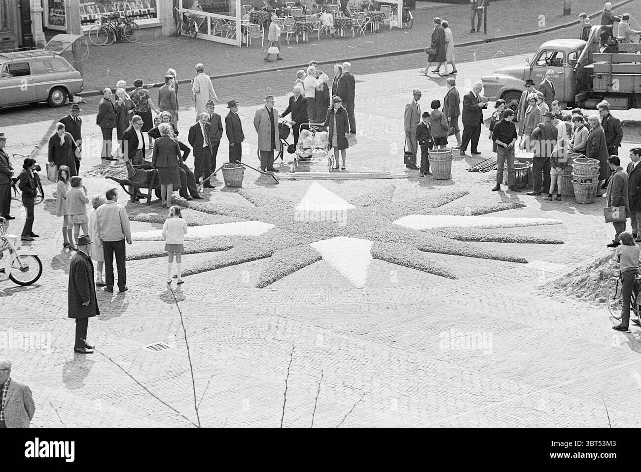 Mosaïque de fleurs Grote Markt Grote Markt Haarlem Grote Markt pays-Bas, Whizgle News, Dutch Desk, pays-Bas, 1950 - 2000 on 24-04-1968. Ces rubriques apparaissent dans l'image. La scène capture une place publique animée remplie d'un groupe diversifié de personnes. Au centre, un grand motif en forme d'étoile fait de fleurs ou de matériaux colorés attire l'attention, rayonnant à partir d'un point circulaire. Le blanc vif et plus sombre de la conception contraste avec les tons terreux environnants de la chaussée et les couleurs vibrantes de l'arrangement floral. Entourant cette pièce maîtresse, des groupes d'individus en Banque D'Images