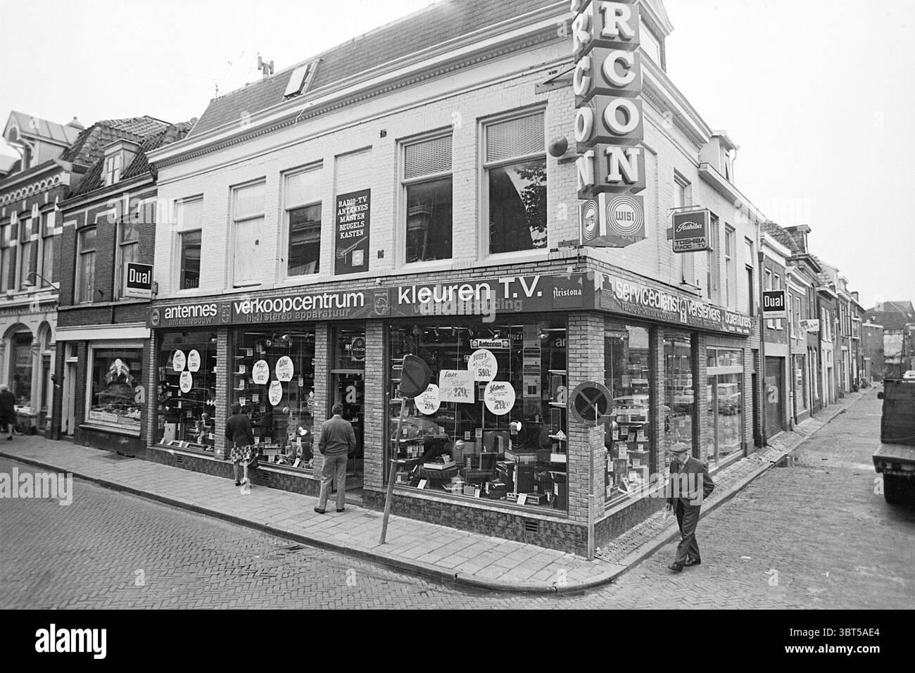 Extérieur Marcon extérieur Haarlem Barrevoetestraat pays-Bas, Whizgle News, Dutch Desk, pays-Bas, 1950 - 2000 le 07-08-1974. Ces rubriques apparaissent dans l'image. La scène représente un coin de rue urbain animé où un magasin de premier plan occupe le rez-de-chaussée d'un immeuble de deux étages. L'architecture présente un mélange de styles contemporain et traditionnel, mis en valeur par de grandes fenêtres en verre qui servent d'étalages pour divers produits électroniques, y compris des téléviseurs et des équipements audio. La vitrine est ornée de panneaux promotionnels circulaires, mettant en valeur des réductions qui ajoutent un soupçon de v Banque D'Images