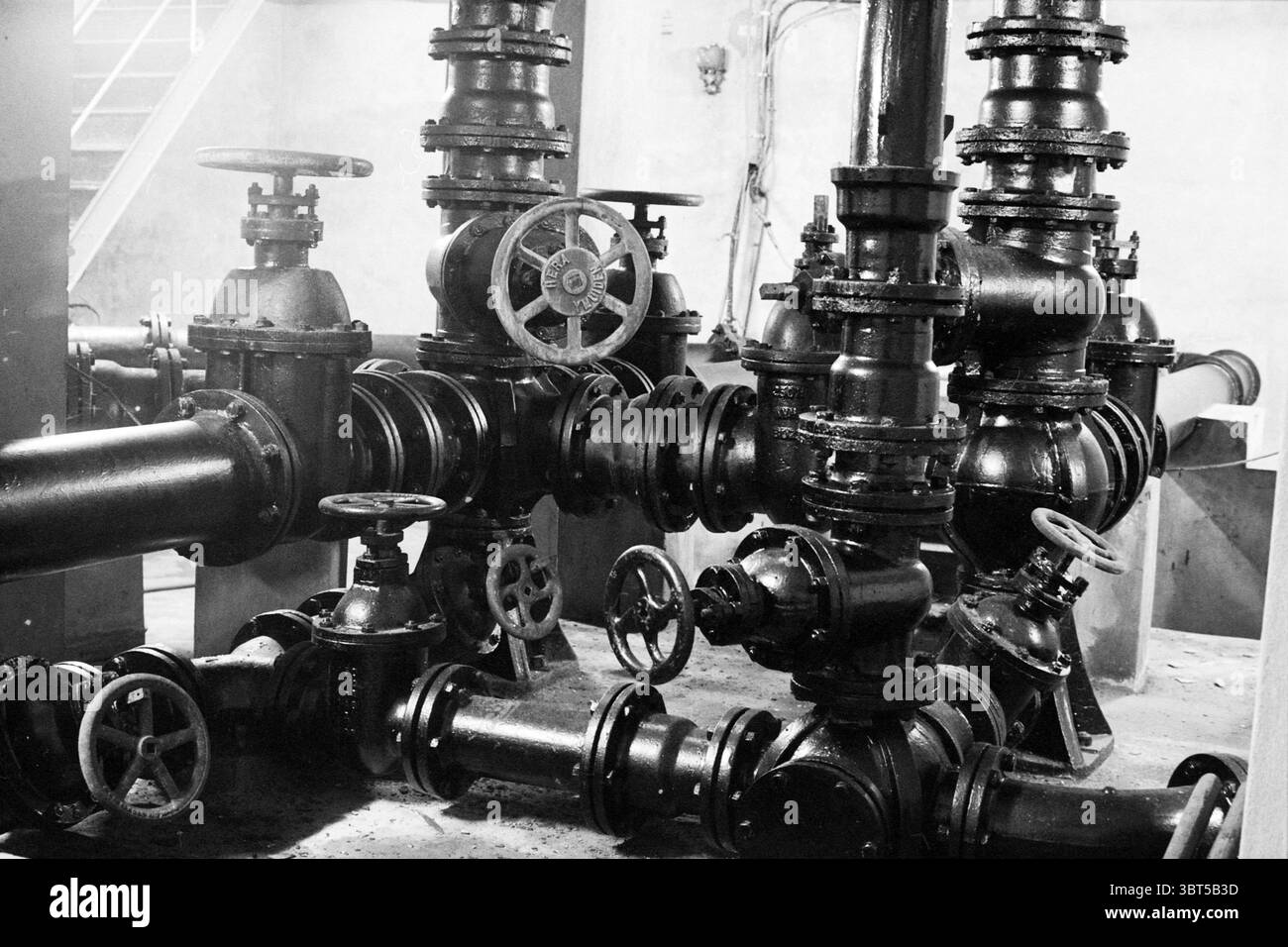Installation dans le château d'eau IJmuiden IJmuiden pays-Bas, Whizgle News, Dutch Desk, pays-Bas, 1950 - 2000 on 04-12-1994. L'image inclut ces rubriques. La scène présente un assemblage dense de tuyauterie industrielle et de machines, caractérisé par un réseau de tuyaux noirs interconnectés par diverses vannes et raccords. La disposition complexe de ces composants crée un sentiment de complexité et de fonctionnalité, avec de nombreuses roues circulaires et leviers, chacun conçu pour le contrôle et le réglage, visibles le long des tuyaux. La palette de couleurs est dominée par des nuances sombres, principalement le noir et Banque D'Images