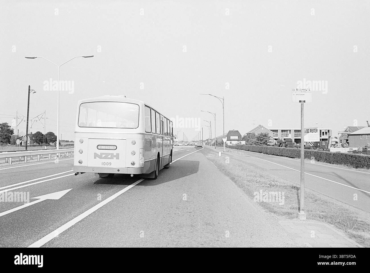 Weg Haarlem - Halfweg Noord Zuid Hollandse Vervoersmaatschappij N.V. NZ Roads Road construction Road planter, Whizgle News, Dutch Desk, pays-Bas, 1950 - 2000 on 04-07-1968. L'image montre ces rubriques. La scène représente un long tronçon de route avec un bus vintage s'éloignant du spectateur. Le bus est principalement blanc avec des accents bleu clair et porte le numéro '1009' affiché bien en évidence à l'arrière. Ses bords arrondis et sa forme générale évoquent un sentiment de nostalgie pour le design du milieu du XXe siècle. À gauche, la route est bordée par une bande d'herbe bien rangée, tandis qu'un arrêt de bus solitaire est visib Banque D'Images