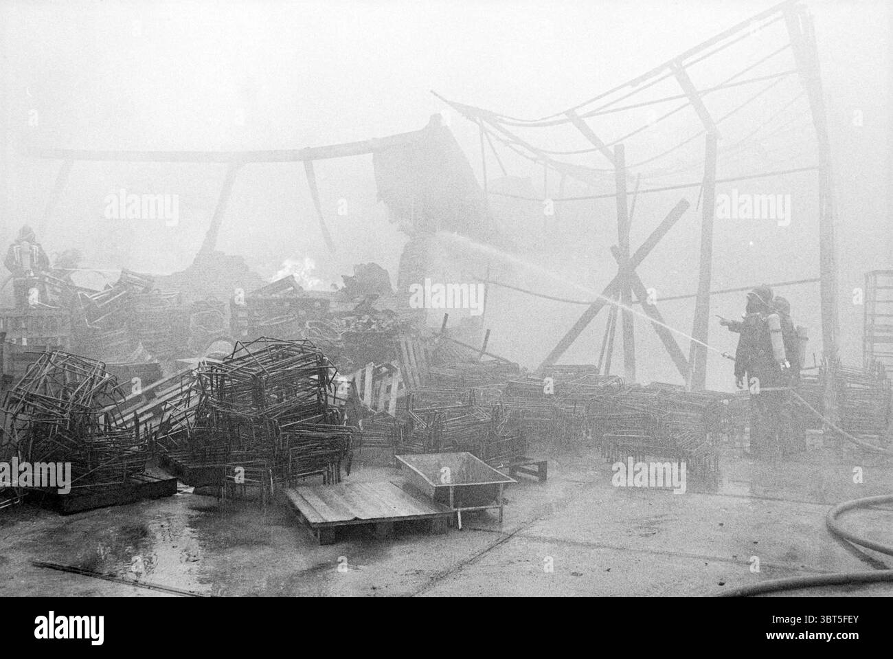 Hangar à ampoules à feu fa. Willemsen Hillegom Fire brigade Hillegom, Whizgle News, Dutch Desk, pays-Bas, 1950 - 2000 on 02-03-1980. L'image montre ces rubriques. Dans une scène entourée d'une brume épaisse, la visibilité est compromise, créant une atmosphère dense de fumée et d'obscurité. Le cadre semble être un site de destruction, peut-être à la suite d'un incendie. Des fragments de structures détruites apparaissent en arrière-plan, leurs contours s'évanouissent et se déforment en raison de la brume épaisse qui enveloppe l'environnement. Dispersés à travers le sol sont de nombreux cadres métalliques, leurs conceptions autrefois fonctionnelles Banque D'Images