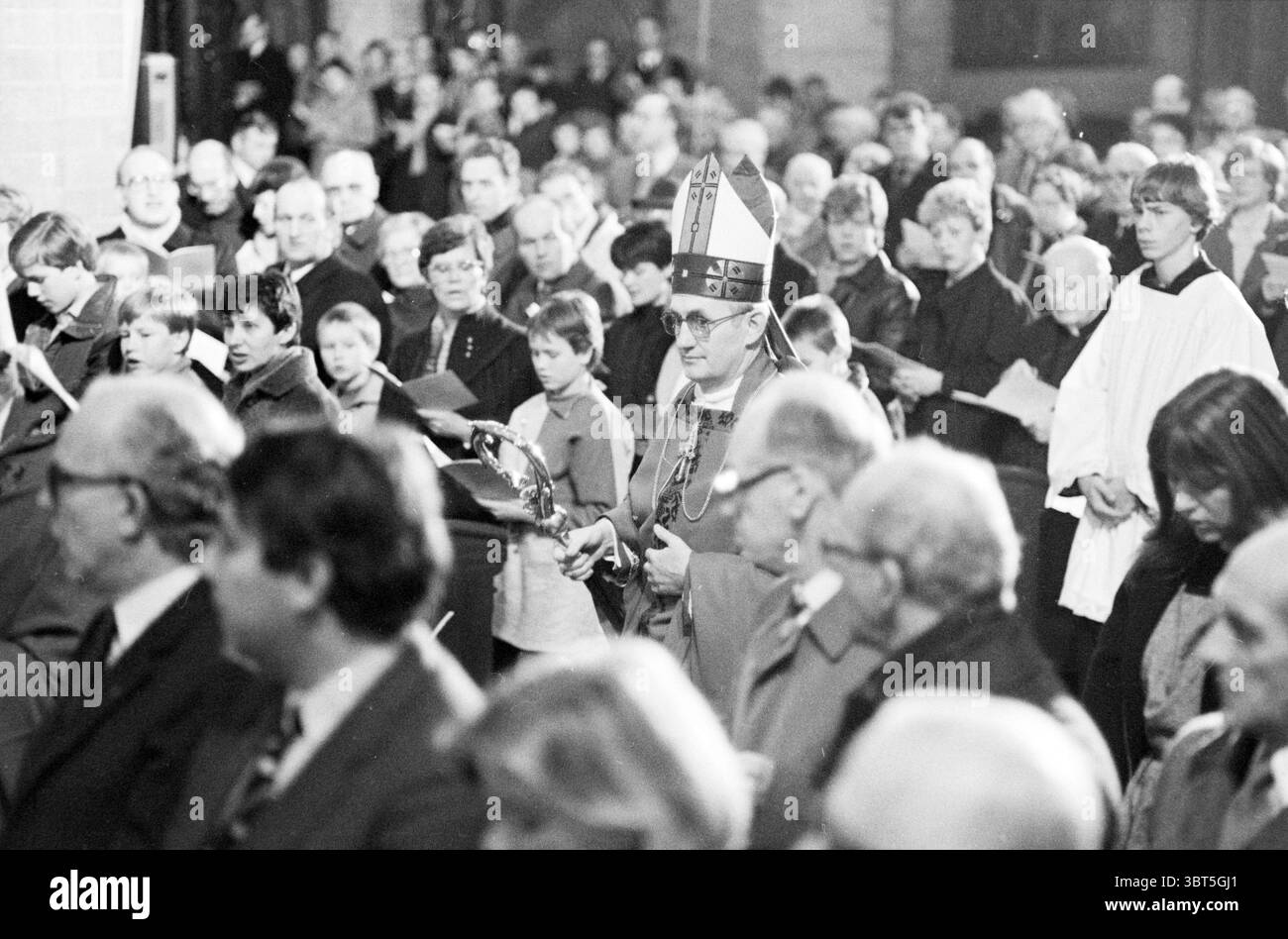 Ordination de l'évêque Bomers et de l'évêque auxiliaire Lescrauwaert RK Bavo Haarlem consécration Église catholique romaine Haarlem pays-Bas, Whizgle News, Dutch Desk, pays-Bas, 1950 - 2000 on 14-01-1984. L'image inclut ces rubriques. La scène est remplie d'un rassemblement dense de gens, tous engagés dans une atmosphère solennelle. À l'avant-garde, une figure vêtue d'une tenue de cérémonie, y compris un grand chapeau orné, se tient au centre de la scène. La présence de cette personne attire l'attention. Ils ont un personnel, révélateur de leur rôle religieux, et sont concentrés sur la congrégation. Entourant cette figu Banque D'Images