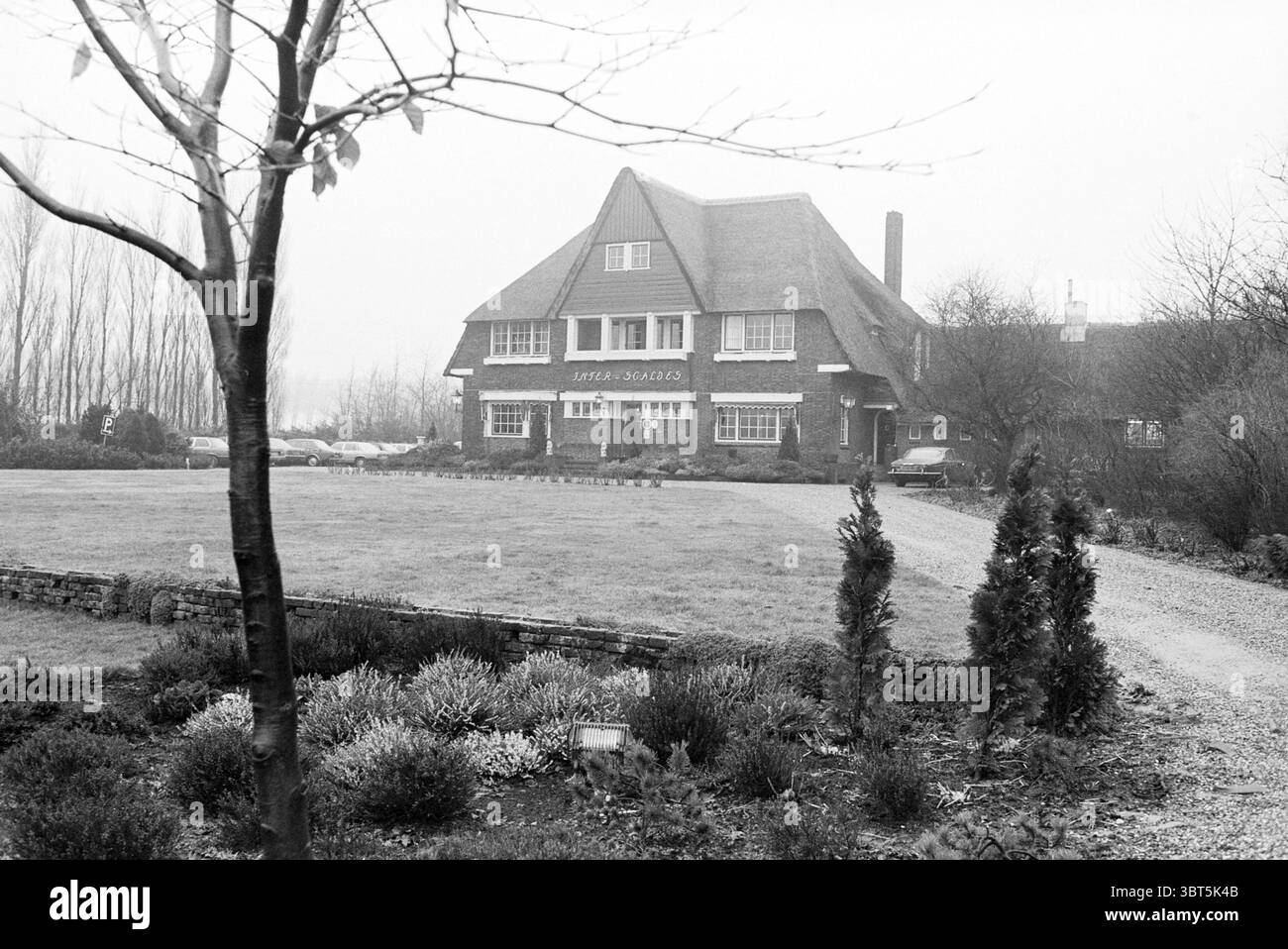 Introduction déjeuner 'Alliance gastronomique néerlandaise' restaurant Inter Scaldes Kruiningen, Whizgle News, Dutch Desk, pays-Bas, 1950 - 2000 le 28-01-1981. Ce sont les éléments de l'image. La scène représente une grande maison de deux étages caractérisée par son architecture distincte. Il dispose d'un toit escarpé et en pente orné de bardeaux, et de fenêtres proéminentes qui donnent sur le niveau supérieur. L'extérieur est fait de briques, donnant un aspect robuste, tandis que les fenêtres, encadrées en blanc, créent un contraste avec la façade plus sombre. Autour de la maison est une pelouse spacieuse, qui a Banque D'Images