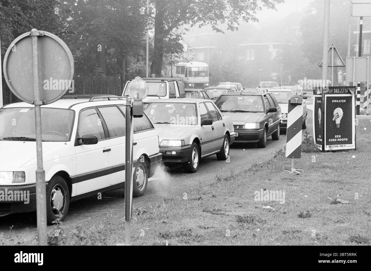 Embouteillages devant le pont Buitenrust Haarlem Buitenrustlaan pays-Bas, Whizgle News, Dutch Desk, pays-Bas, 1950 - 2000 on 15-09-1991. L'image montre ces rubriques. La scène présente une chaussée encombrée, avec plusieurs véhicules alignés dans la circulation. Diverses voitures, principalement dans des tons blancs, gris et foncés, sont visibles, indiquant un mélange de modèles plus anciens et plus contemporains. Le cadre semble être une banlieue, comme le suggèrent les bâtiments résidentiels faiblement visibles à travers une couche de brume ou de brouillard. Quelques panneaux de signalisation sont présents, l'un affichant un circ Banque D'Images