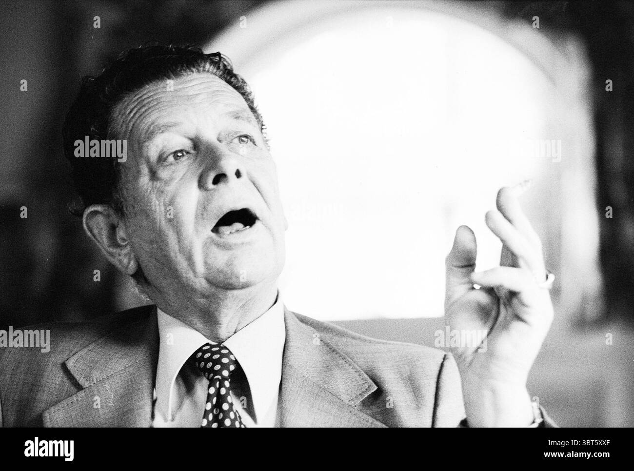 Portraits Willy van Hemert Portraits, Whizgle News, Dutch Desk, pays-Bas, 1950 - 2000 sur 09-01-1980. Voici les rubriques de l'image. La scène représente un homme plus âgé dans un cadre formel, caractérisé par un costume classique qui porte une teinte gris clair, complété par une cravate à pois distinctive. Son expression faciale est animée, avec sa bouche ouverte comme en pleine conversation ou exprimant une pensée perspicace. Les cheveux épais et ondulés du monsieur sont teintés de gris, et il semble avoir un comportement réfléchi, avec des yeux profonds qui attirent l'attention. Sa main gauche est levée, les doigts légers Banque D'Images