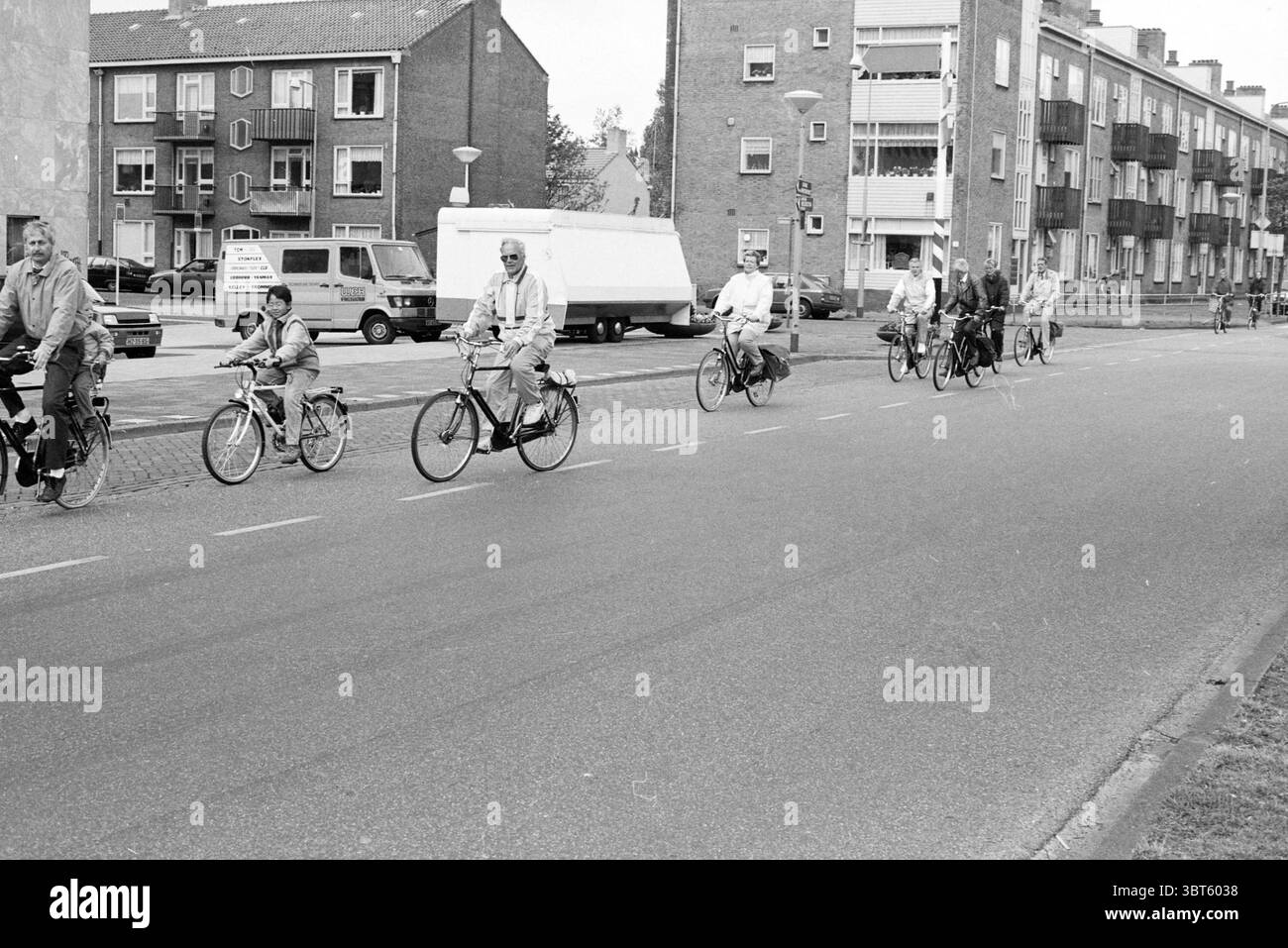 Journée cycliste nationale départ de la place du marché pistes cyclables cyclistes Marktplein, Whizgle News, Dutch Desk, pays-Bas, 1950 - 2000 le 13-05-1989. Voici les rubriques de l'image. La scène représente un groupe d'individus faisant du vélo le long d'une large route pavée qui s'étend en arrière-plan. Ils font du vélo dans une seule file, suggérant un rythme tranquille. Les cyclistes sont un mélange d'âges, avec des adultes et un enfant bien en vue, démontrant un sens de la communauté et de la vie quotidienne. Les environs comprennent plusieurs bâtiments résidentiels, caractérisés par un utilitaire de Banque D'Images