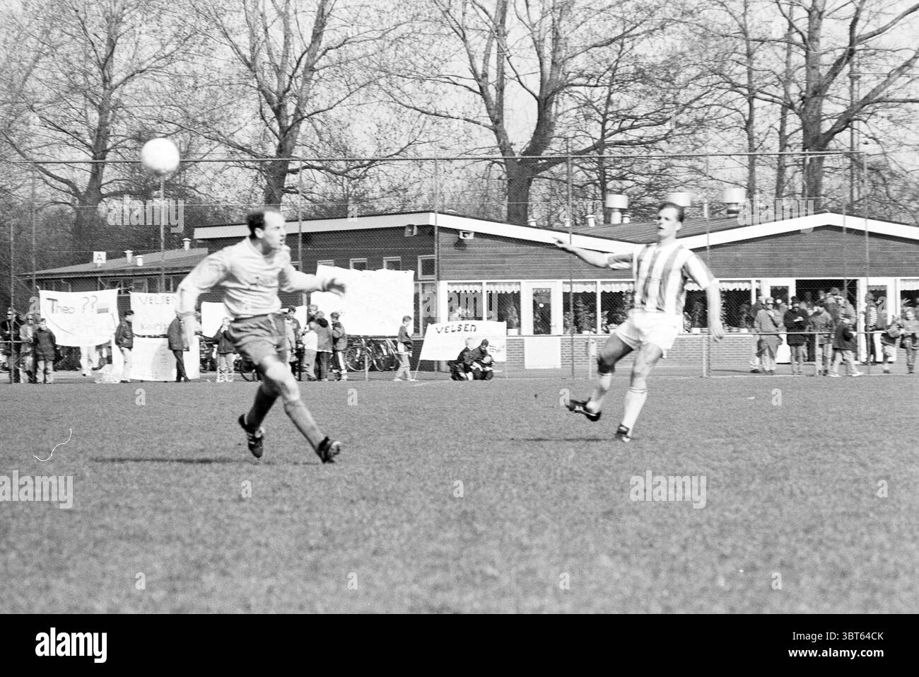 Velsen - Waterloo, Whizgle News, Dutch Desk, pays-Bas, 1950 - 2000 le 01-04-1995. L'image contient ces rubriques. La scène capture un moment intense dans un match de football se déroulant sur un terrain herbeux. Au premier plan, deux joueurs sont engagés dans un jeu dynamique. Un joueur, vêtu d'un uniforme de couleur claire avec des rayures horizontales, est en plein air essayant de frapper une balle. Sa posture est athlétique et concentrée, transmettant l'effort et la détermination du jeu. L'autre joueur, portant un uniforme plus sombre, semble être en poursuite, avec une expression concentrée lorsqu'il se positionne Banque D'Images