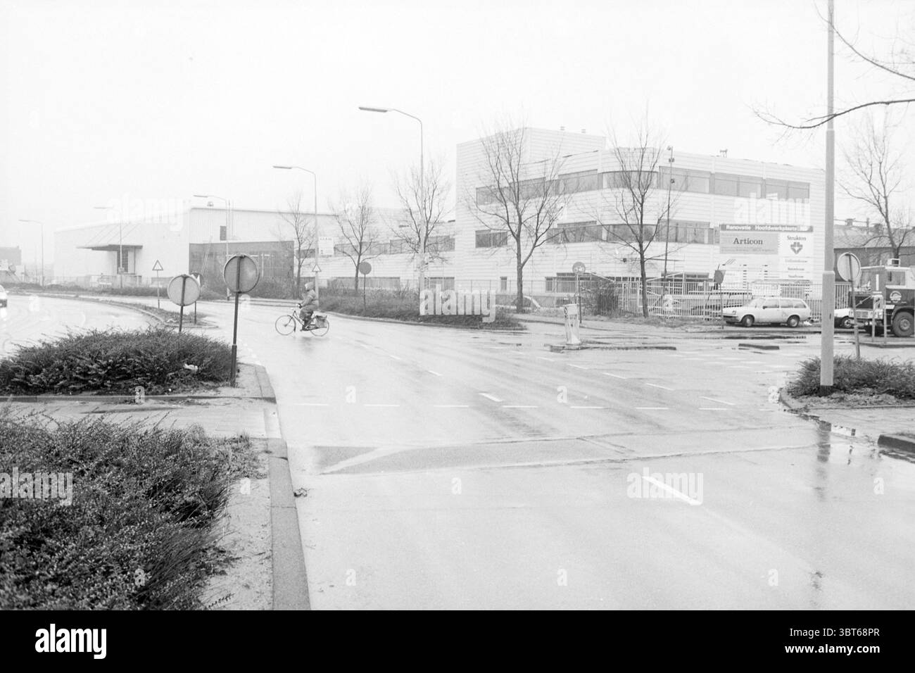 Extérieur NS building Oudeweg Railways Haarlem Oudeweg pays-Bas, Whizgle News, Dutch Desk, pays-Bas, 1950 - 2000 on 09-12-1985. L'image inclut ces rubriques. La scène capture un jour sombre et couvert, enveloppé d'une lumière douce et silencieuse qui confère une sensation de calme et d'immobilité. Le cadre comprend une zone industrielle, caractérisée par de grands bâtiments utilitaires avec une façade principalement grise. Les structures possèdent un design moderne, avec des toits plats et de grandes fenêtres, bien que la visibilité soit quelque peu obscurcie par la brume et le brouillard qui persistent dans l'air. Au premier plan, un Banque D'Images