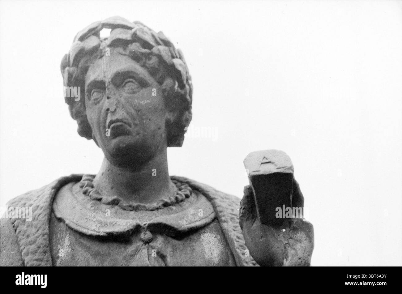 Image battue, Whizgle News, Dutch Desk, pays-Bas, 1950 - 2000 sur 11-1981. L'image montre ces rubriques. La scène présente une statue altérée, fabriquée en pierre sombre ou peut-être en bronze, lui donnant un aspect vieilli et texturé. La figure se tient fièrement mais porte des signes d'usure, tels que de petites fissures et une décoloration. La statue représente une figure solennelle, probablement représentant un personnage historique ou mythique, avec un sourcil sillonné qui suggère la sagesse ou la contemplation. La tête est ornée d'une couronne de laurier, signe de triomphe ou d'honneur. L'expression sur le visage est grave, transmettant Banque D'Images
