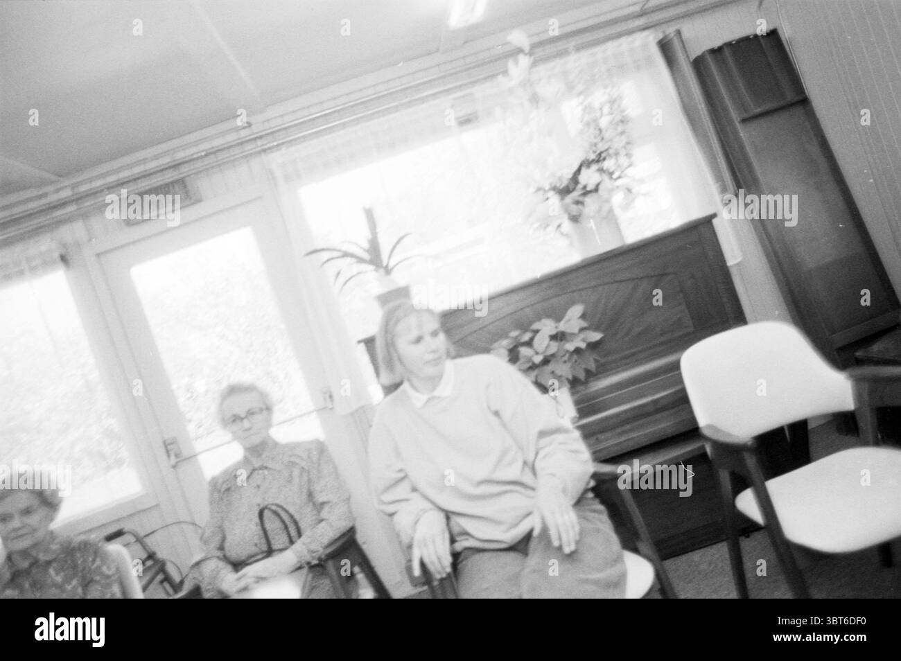 Maire en visite MRS Shoemaker maison de 100 ans Meerstede Hoofddorp Hoofddorp pays-Bas, Whizgle News, Dutch Desk, pays-Bas, 1950 - 2000 le 09-04-1999. L'image montre ces rubriques. Dans un espace intérieur légèrement éclairé, trois personnes sont assises sur de simples chaises, créant une scène qui transmet un sentiment de contemplation tranquille. La salle dispose de grandes fenêtres, permettant à la lumière naturelle de filtrer, projetant de douces ombres sur le sol et les meubles. Les murs et le mobilier sont dans des tons discrets, principalement blancs et gris doux, améliorant l'atmosphère sereine. A gauche, une femme plus âgée Banque D'Images